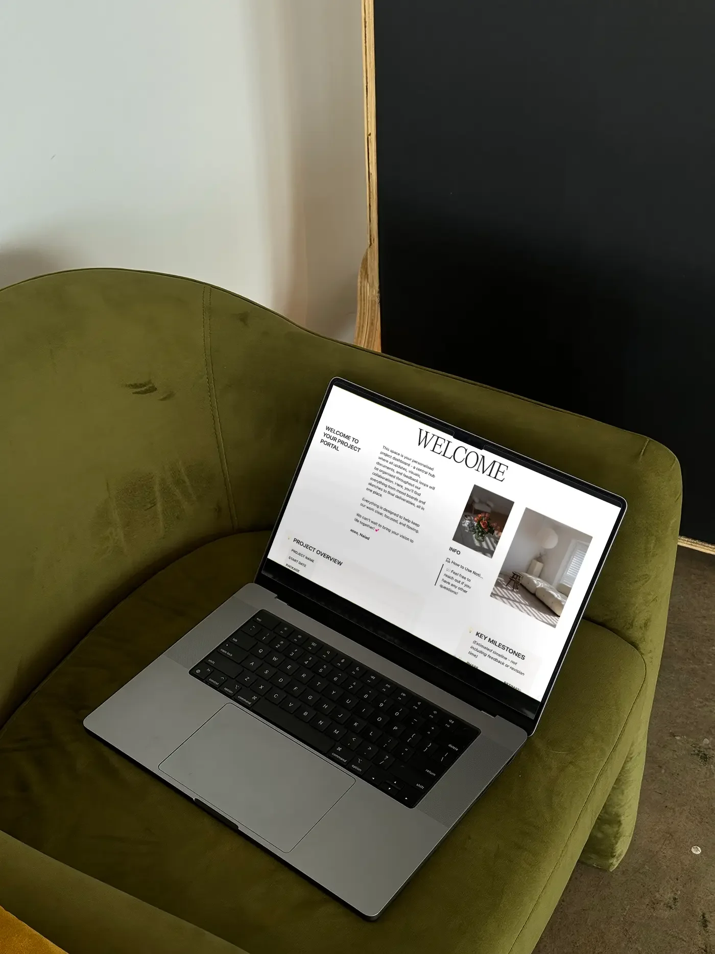 A silver laptop with a black keyboard and a trackpad resting on a green velvet sofa, displaying a welcome webpage for a project.