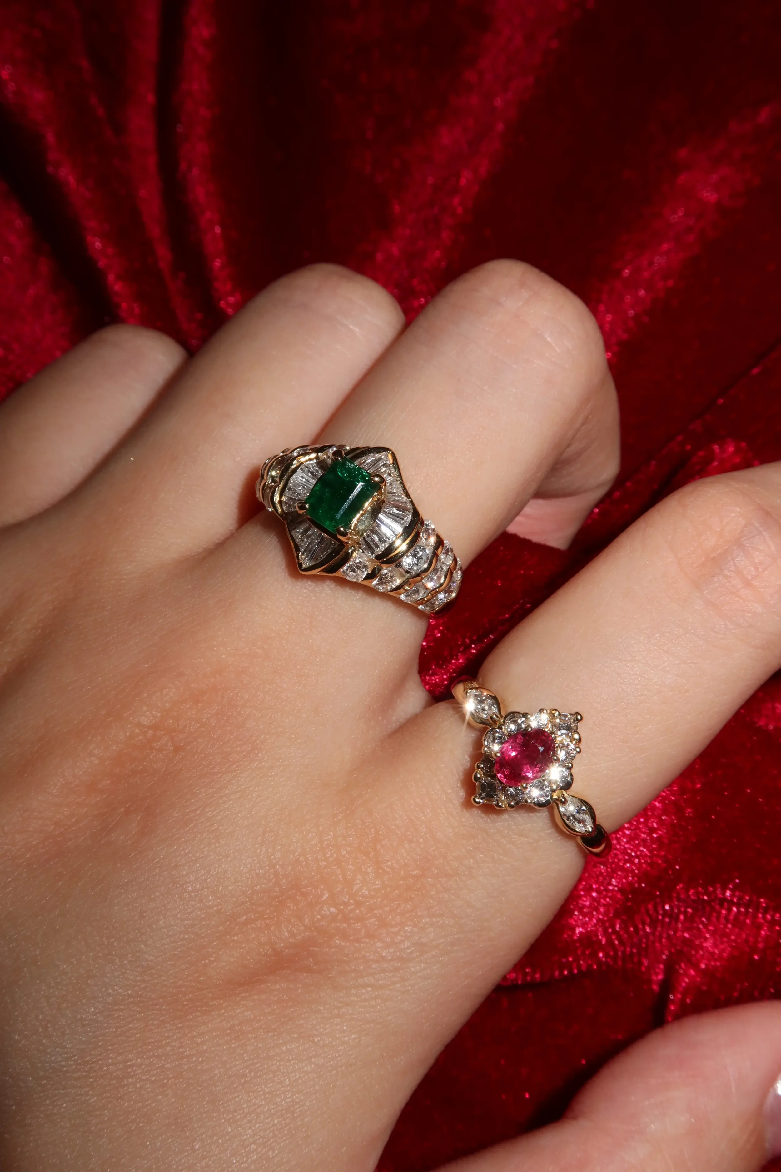 Close-up of a hand wearing two rings with colorful gemstones, set against a red velvet background.