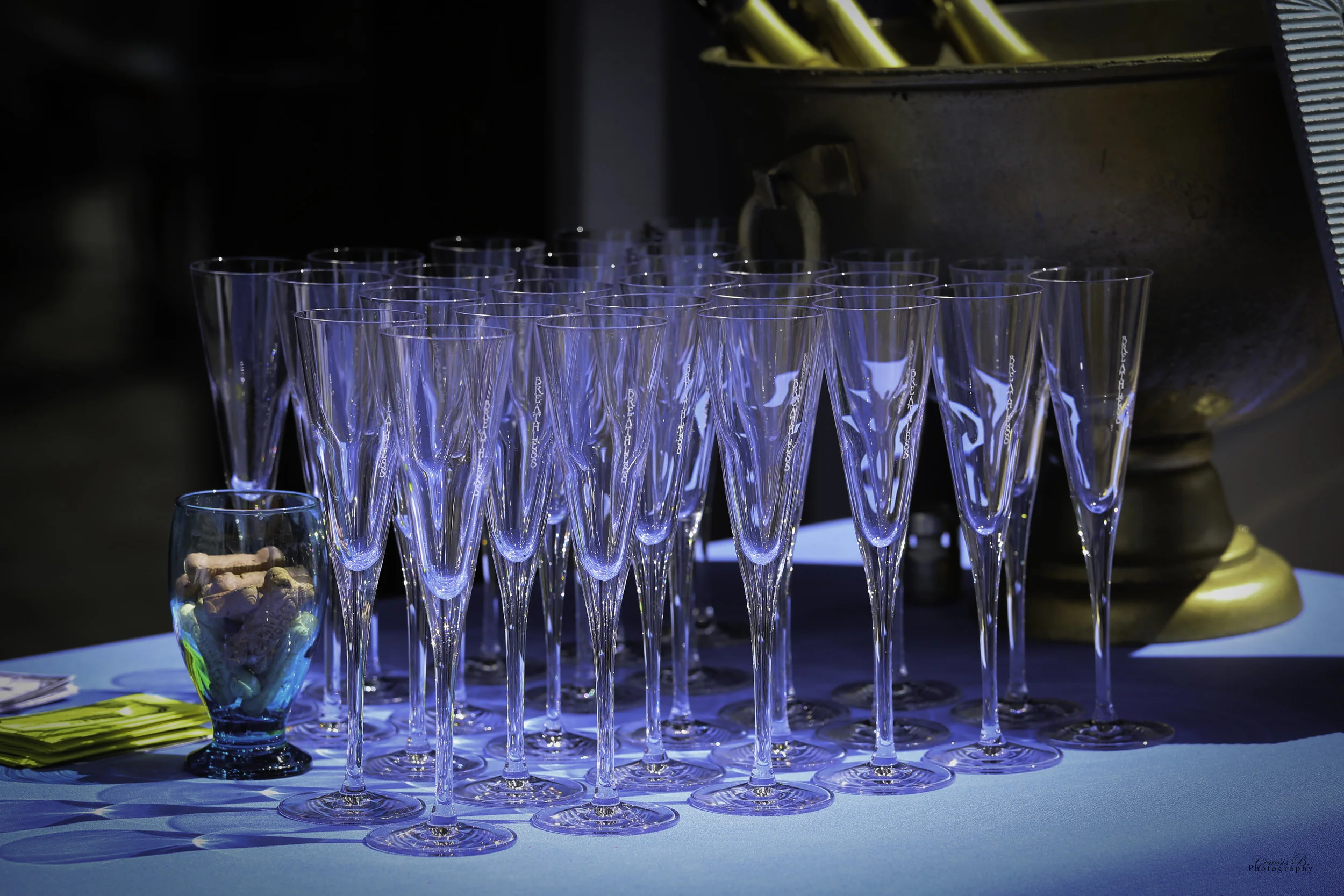 A table with numerous empty champagne flutes and a small bowl filled with candies, in a setting with blue lighting.