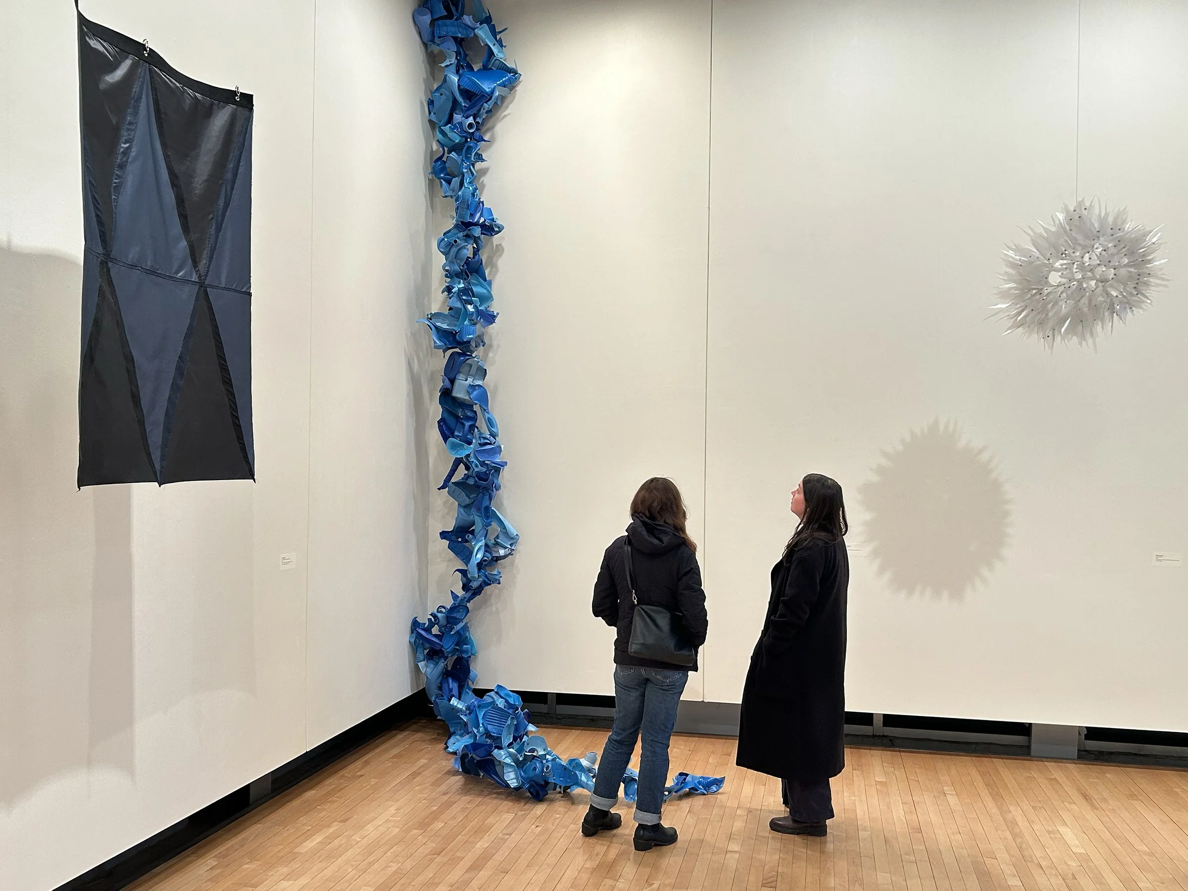 Two people viewing long blue sculpture made of plastic.
