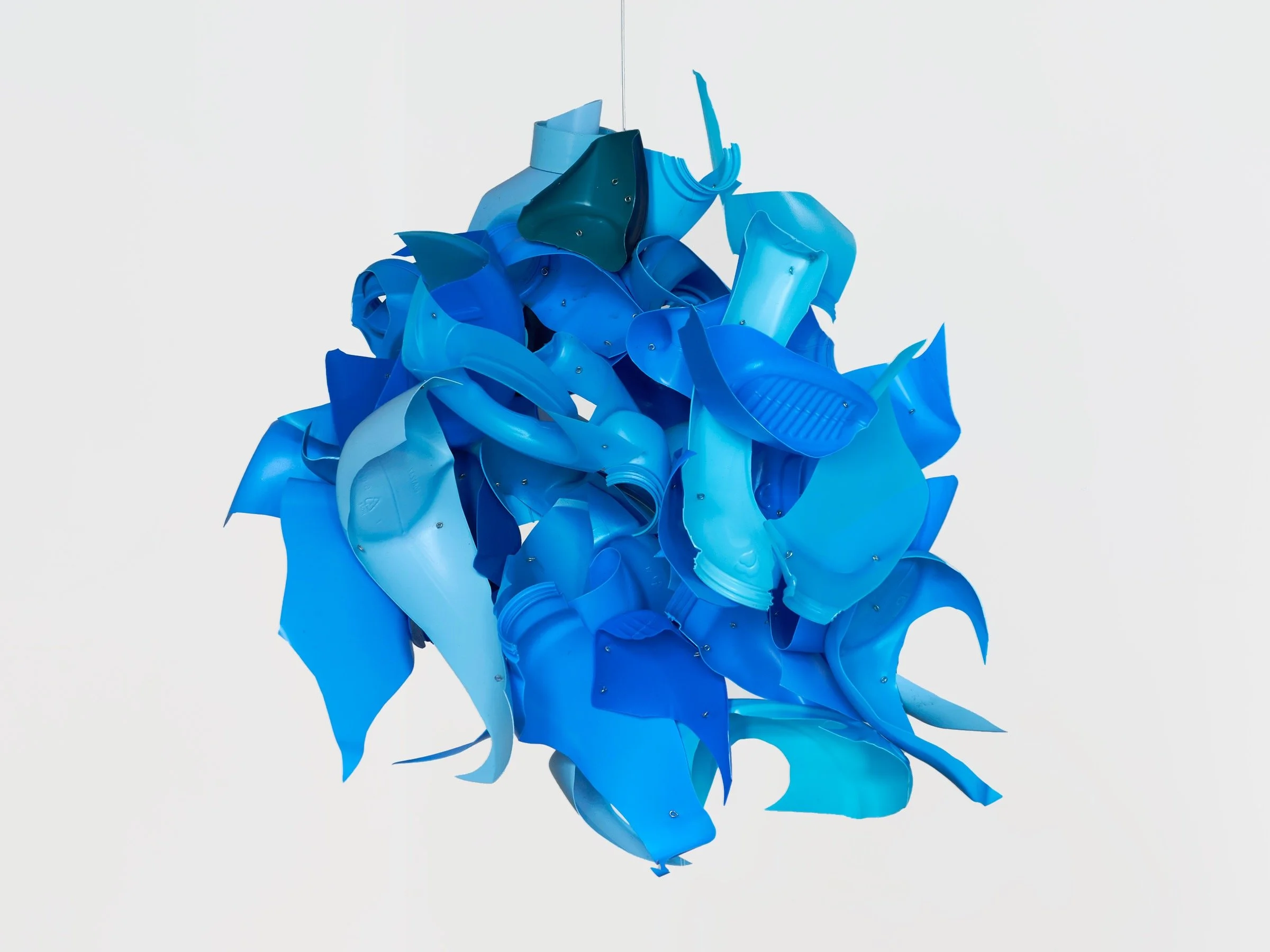 A sculpture made from brightly colored plastic pieces, primarily in shades of blue, arranged in a chaotic, abstract form against a plain white background.