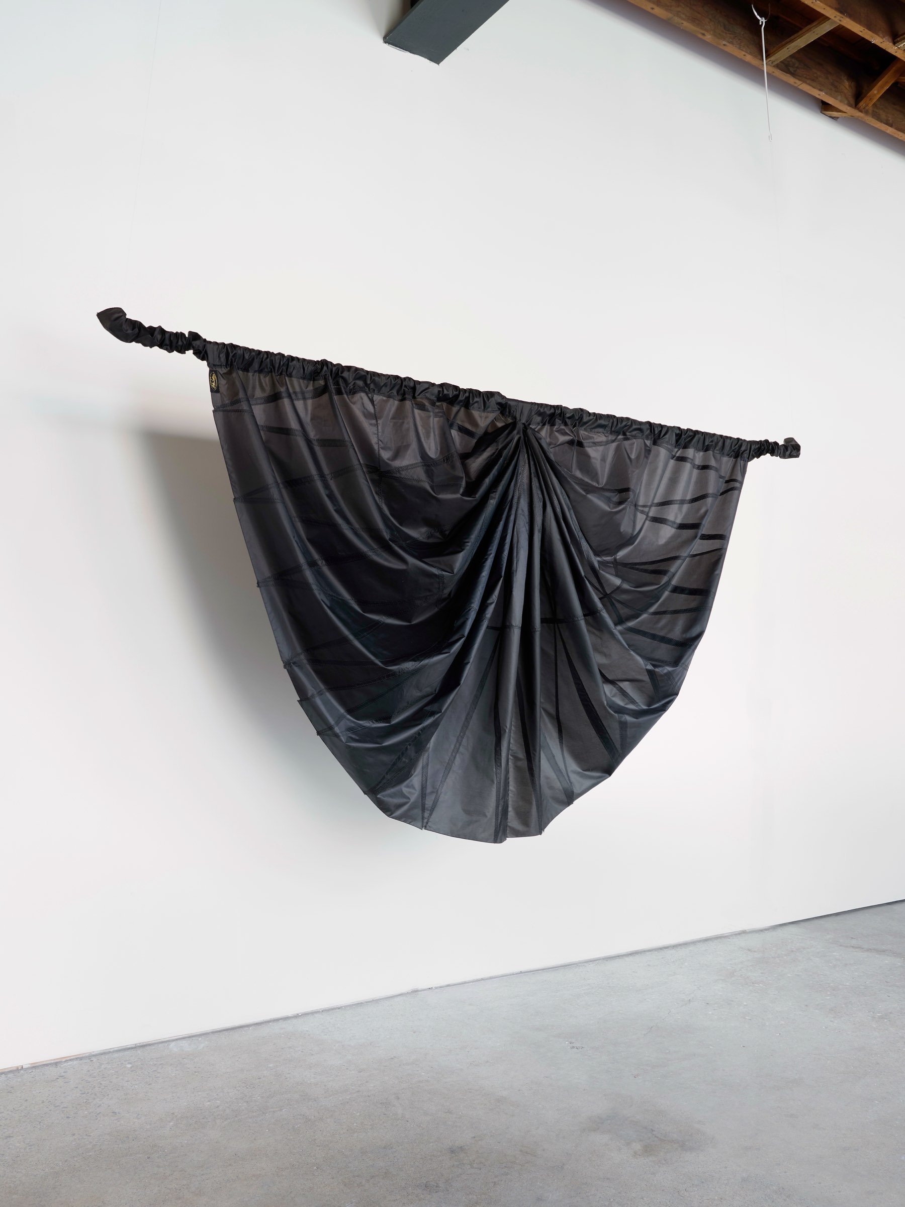 Big Mourning, suspended sculpture of black umbrella canopy material hanging in a soft folded arc against a white wall