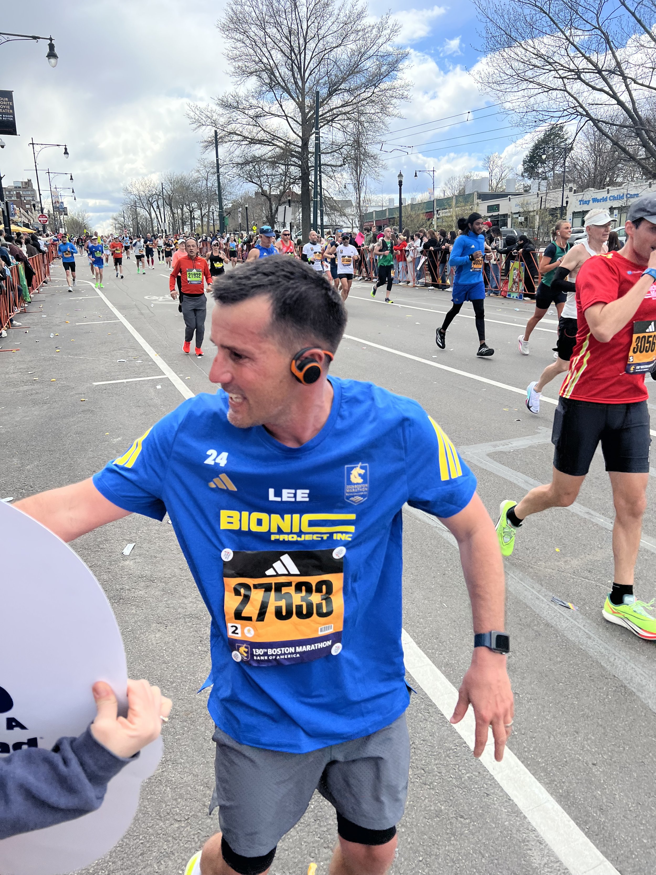 Lee, wearing a blue Bionic Project jersey, reaches toward supporters during the 2026 Boston Marathon.
