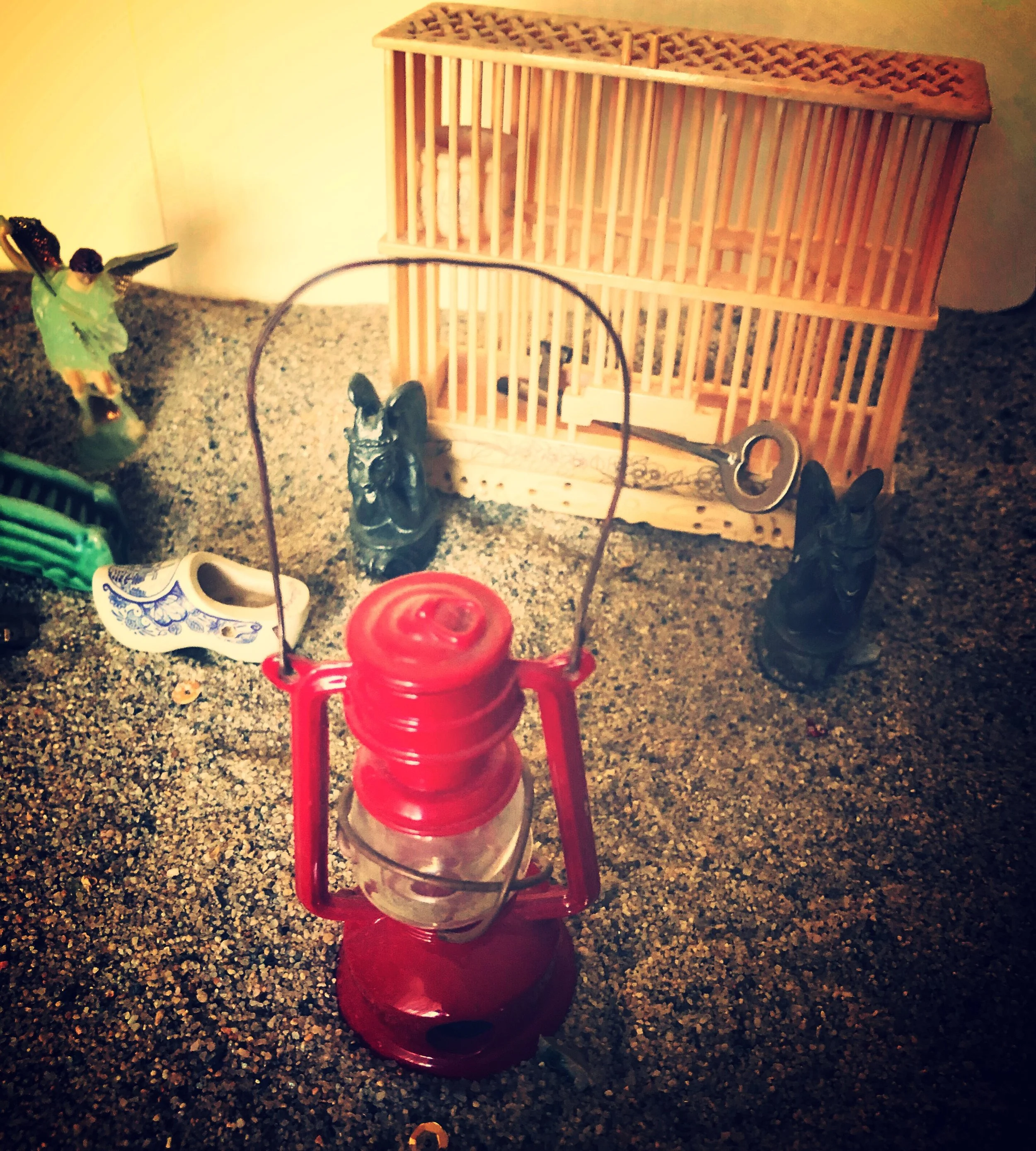 Close up image of a sandbox with a lantern, a wooden cage, and an empty shoe
