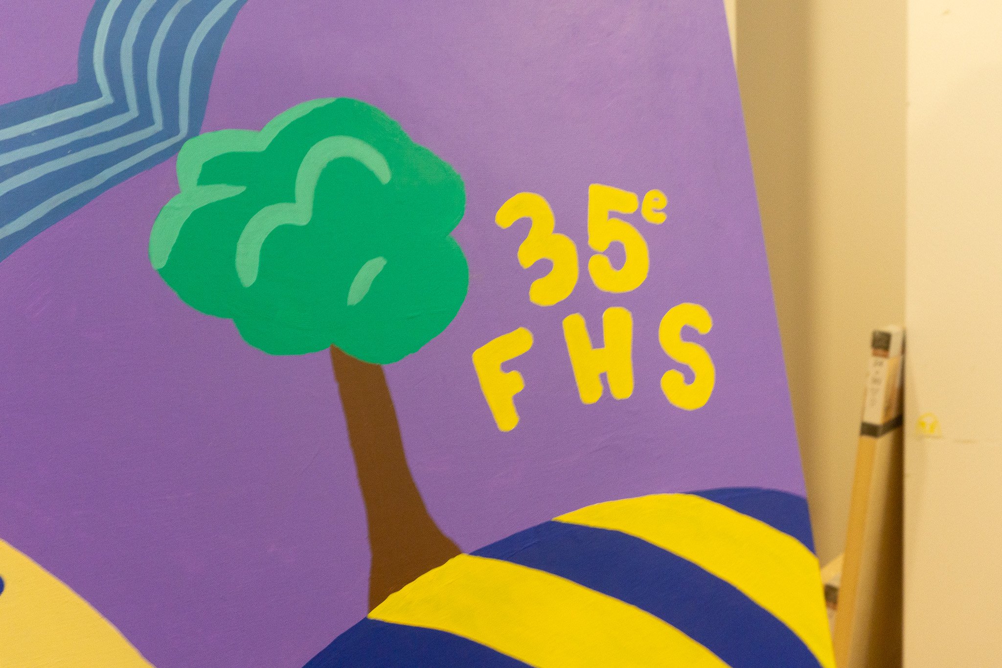 Peinture murale avec un arbre vert stylisé sur fond violet, texte "35e FHS" en jaune, et motifs colorés.