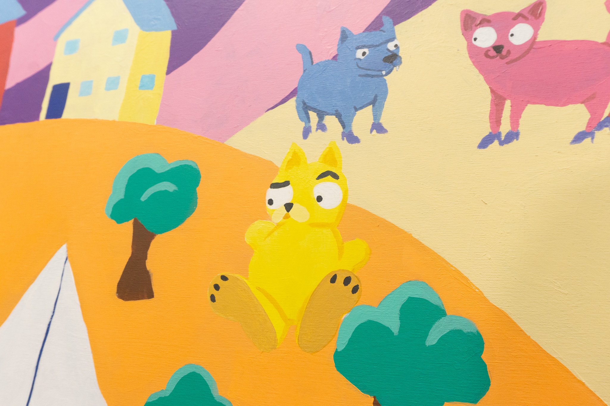 Peinture murale d'animaux stylisés colorés, avec un animal jaune assis et deux animaux bleus et roses en arrière-plan, sur un fond de maisons et arbres stylisés.