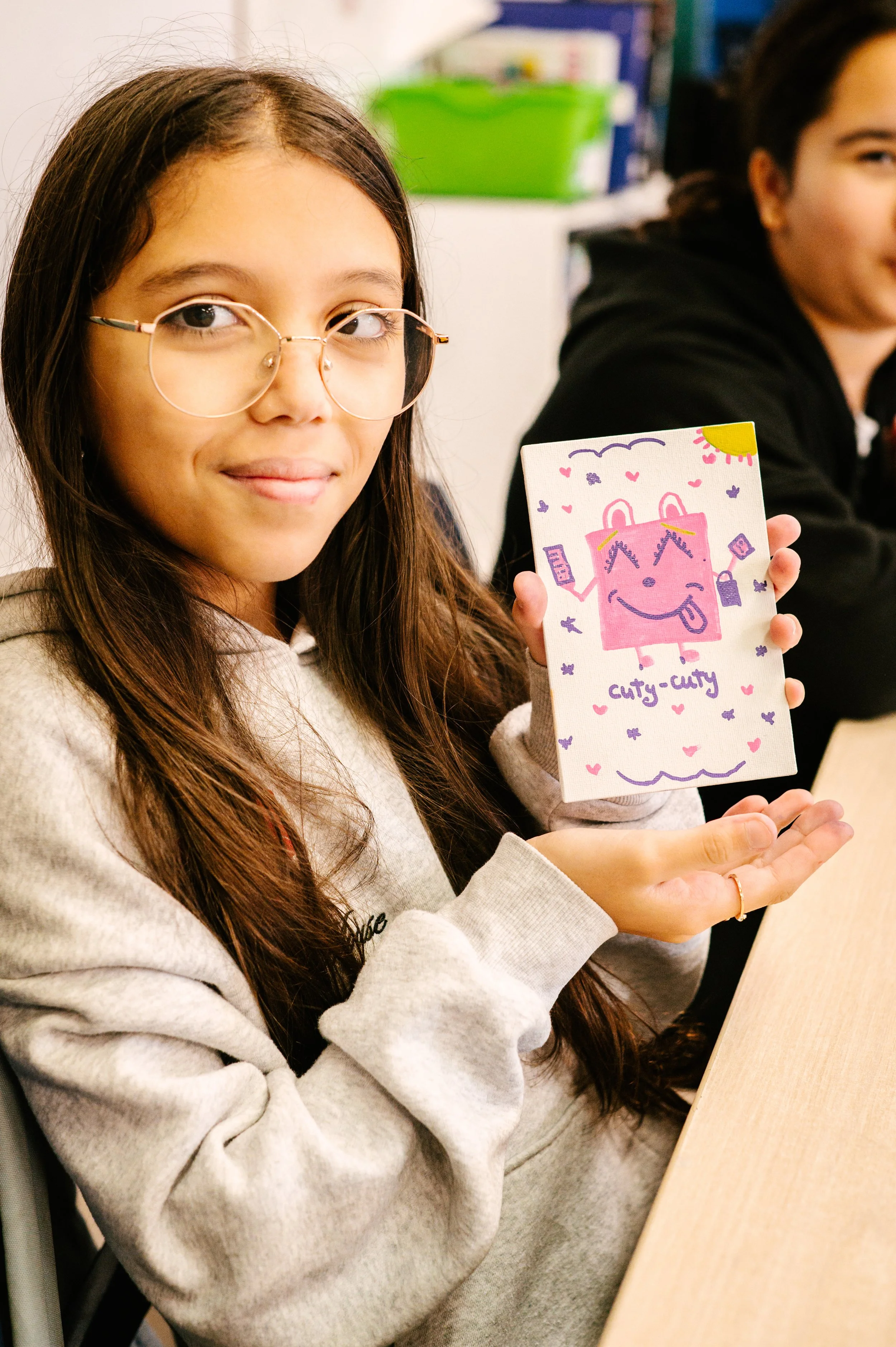 Jeune fille tenant un dessin coloré avec un personnage mignon et les mots "cuty-cuty". Atelier fait par edgar artiste peintre pour l'école primaire jean 23