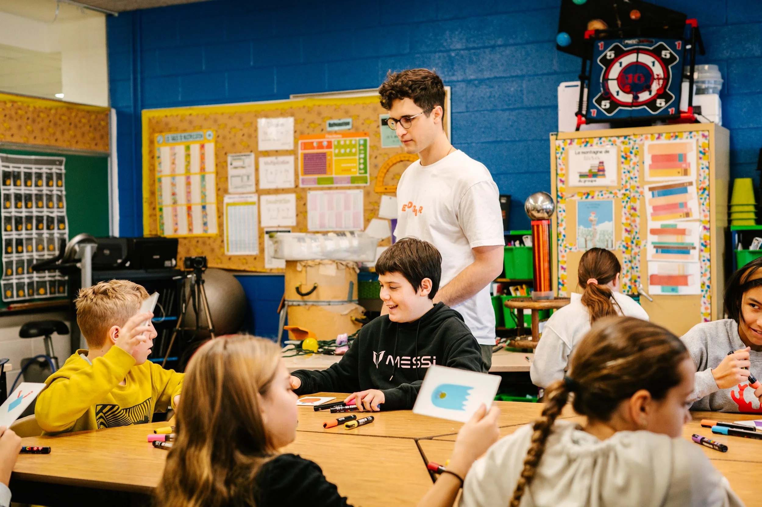 Classe d'enfants et un adulte travaillant ensemble autour d'une table, avec des affiches éducatives au mur. Atelier fait par edgar artiste peintre pour l'école primaire jean 23