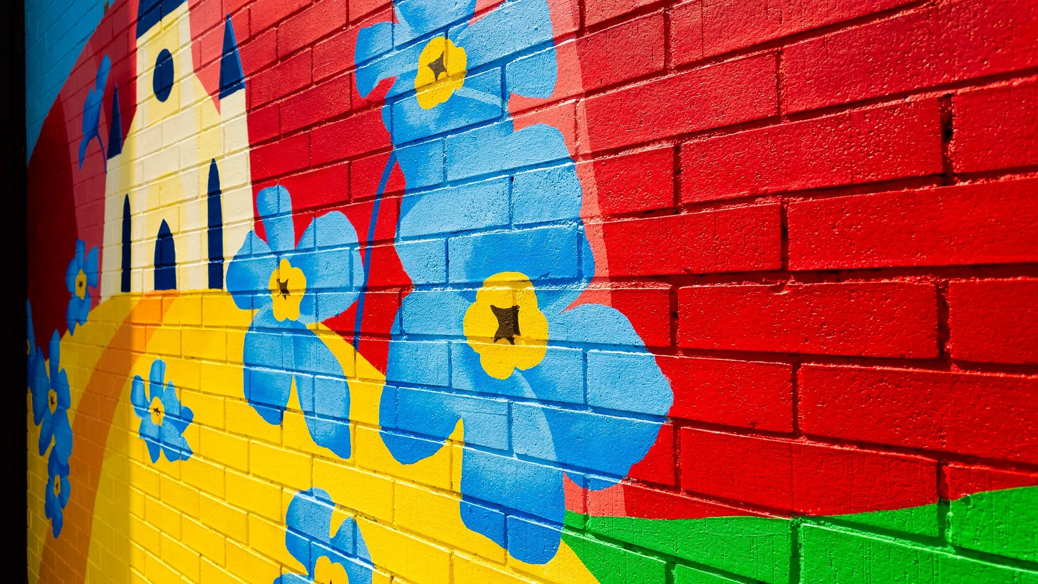 Mural coloré de fleurs bleues avec centres jaunes et pétales bleus sur un mur en briques rouges.