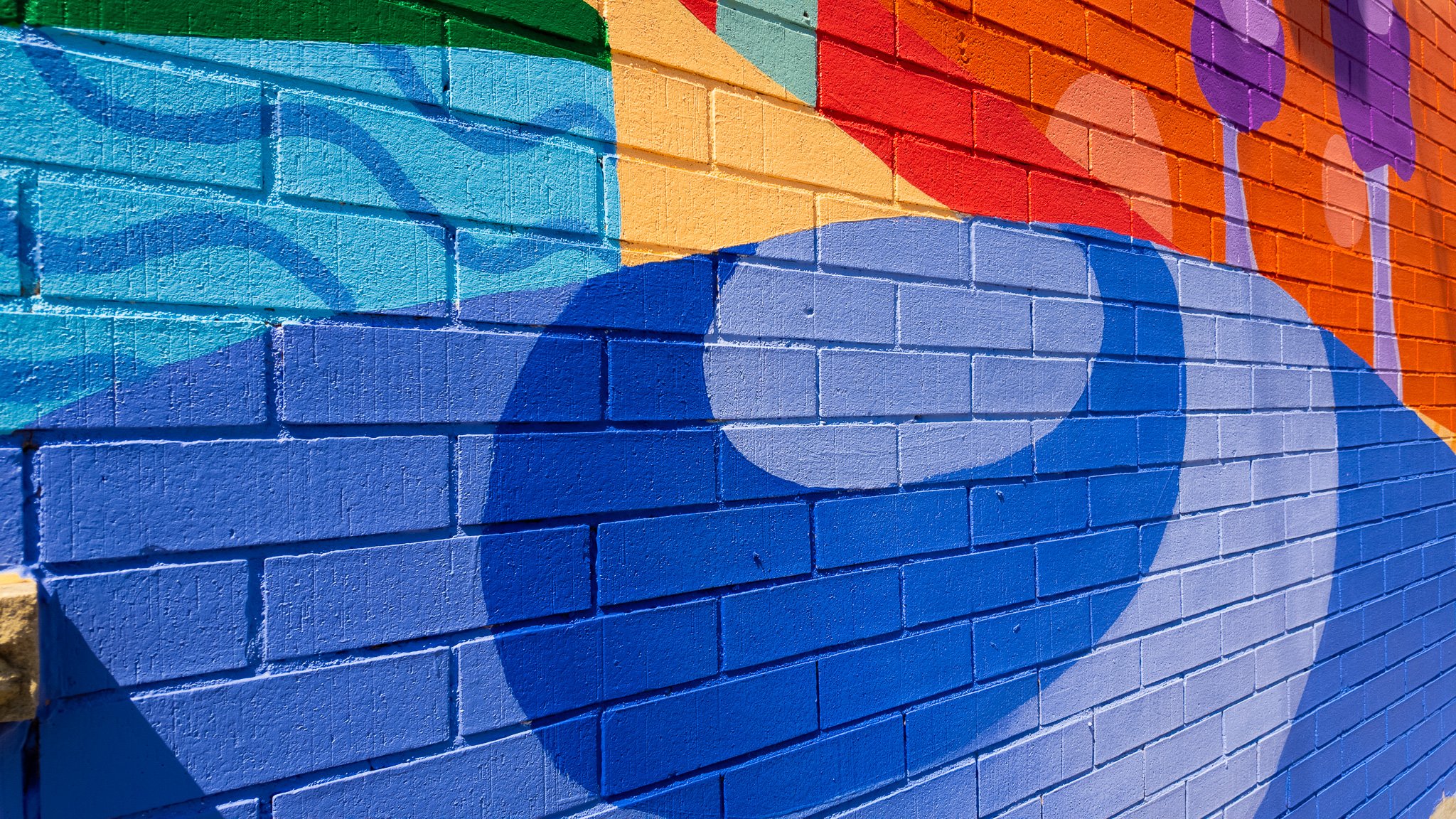 Un mur en briques peint avec un graffiti coloré représentant des cercles et des formes abstraites dans des couleurs vives.