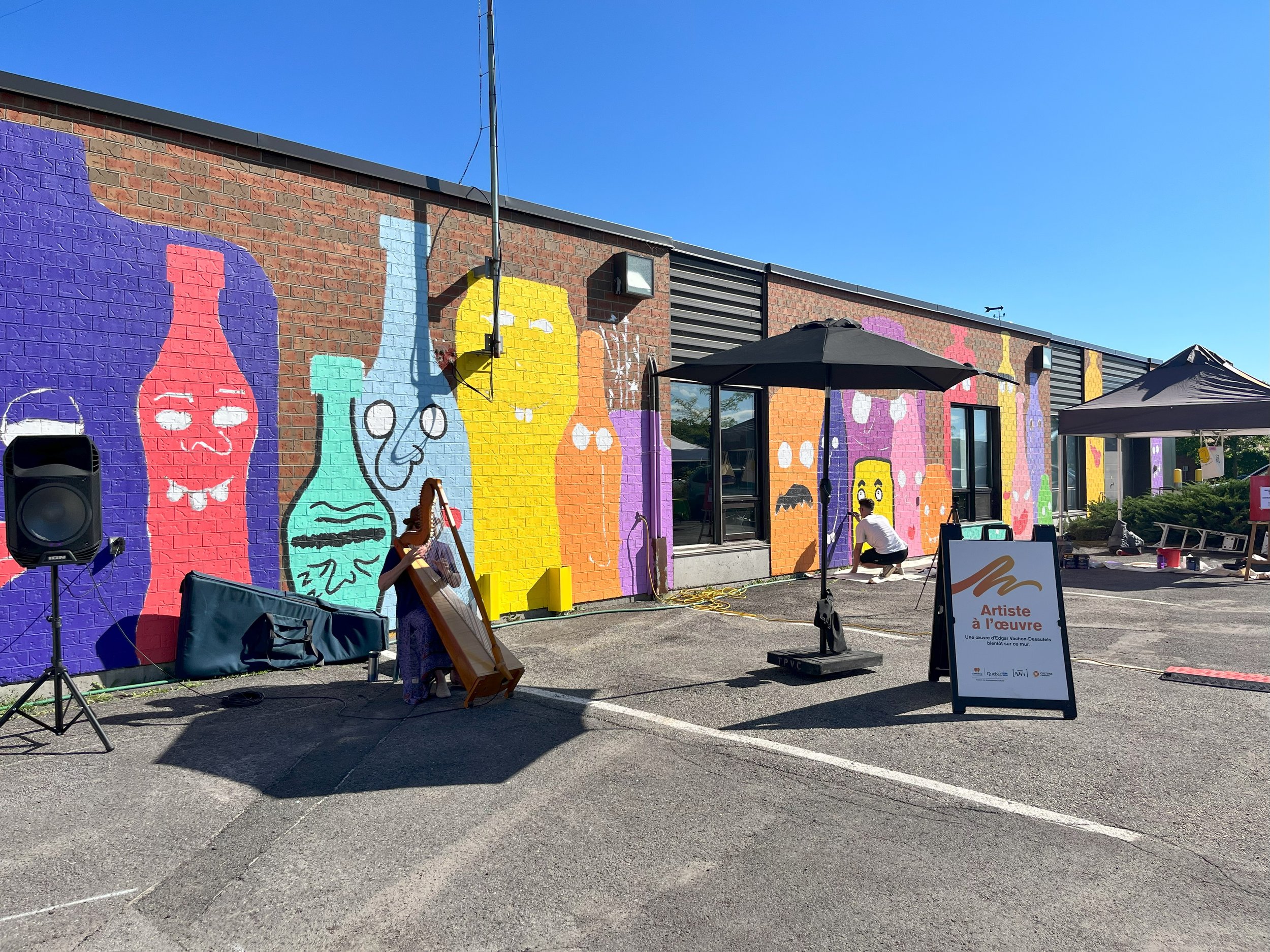 edgar artiste muraliste entrain de peindre la murale la famille des verres durant le marché bio local à candiac