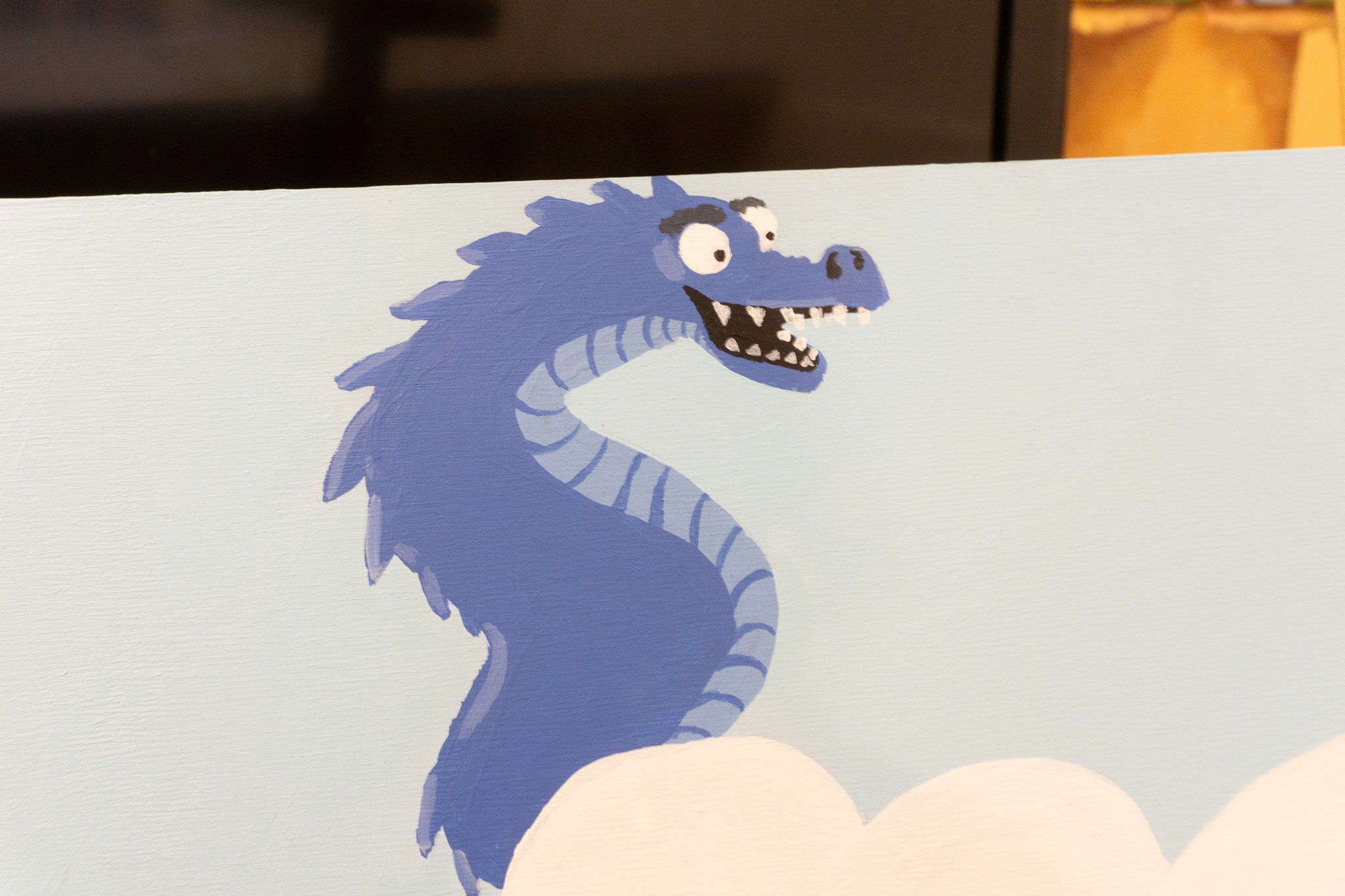 Illustration d'un dragon bleu avec une expression amusante, partiellement caché derrière des nuages, sur fond bleu clair.