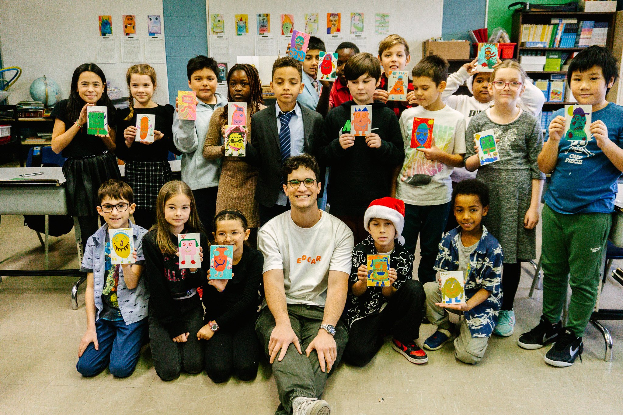 Un groupe d'enfants et un adulte posent dans une salle de classe, chacun tenant un dessin coloré. Atelier fait par edgar artiste peintre pour l'école primaire jean 23