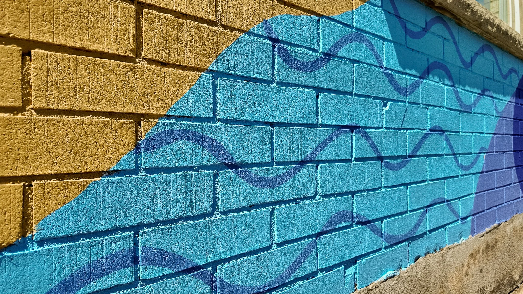 Mural peint sur un mur en briques, avec des couleurs bleu et jaune, représentant des formes abstraites et des lignes ondulées.