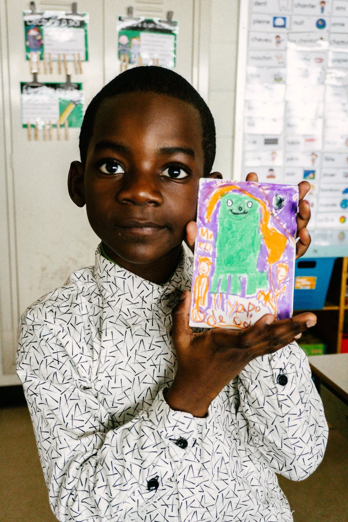 Enfant tenant un dessin coloré avec un personnage vert. Atelier fait par edgar artiste peintre pour l'école primaire jean 23