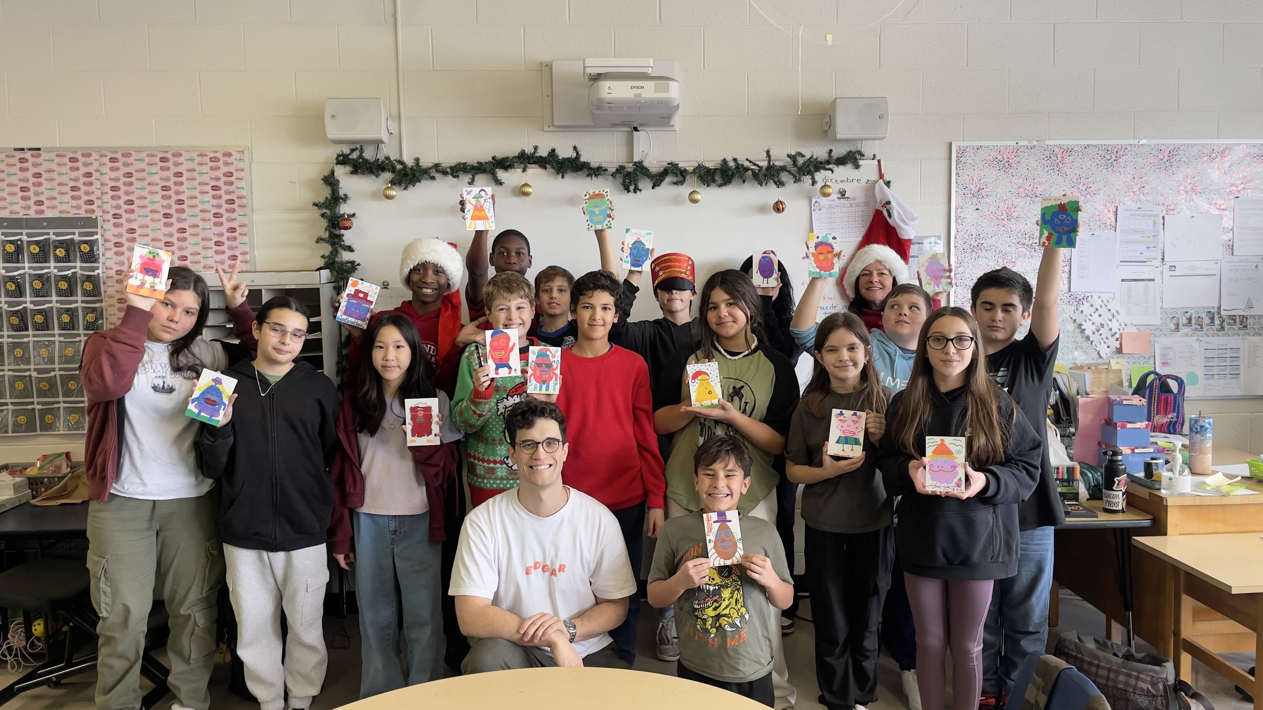 Groupe d'élèves et un adulte, tenant des cartes ou des dessins dans une salle de classe décorée pour les fêtes.