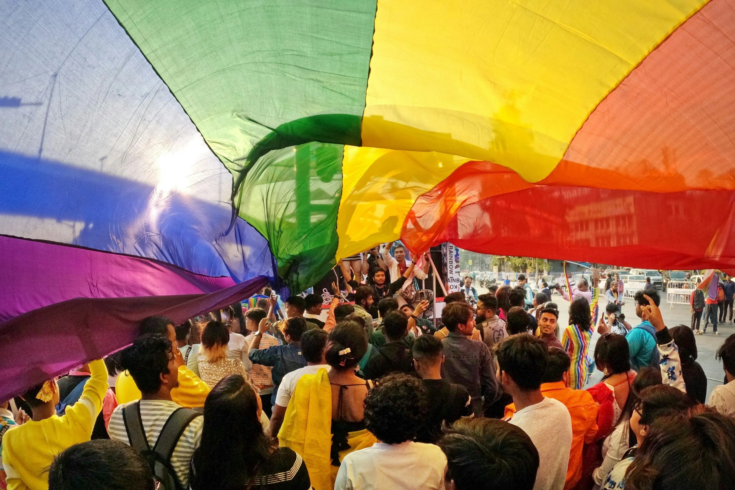 a group of people marching under a large rainbow pride flag