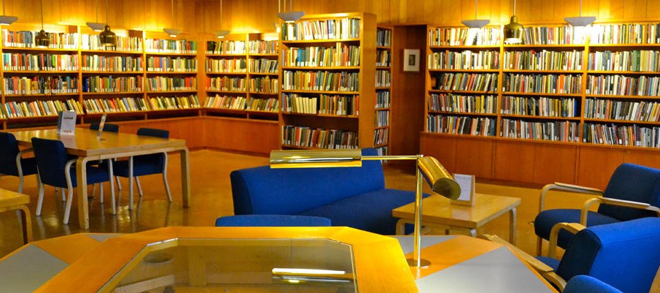 A photo of the Woodberry Poetry room, a wooden library with tables and bookshelves along the wall.