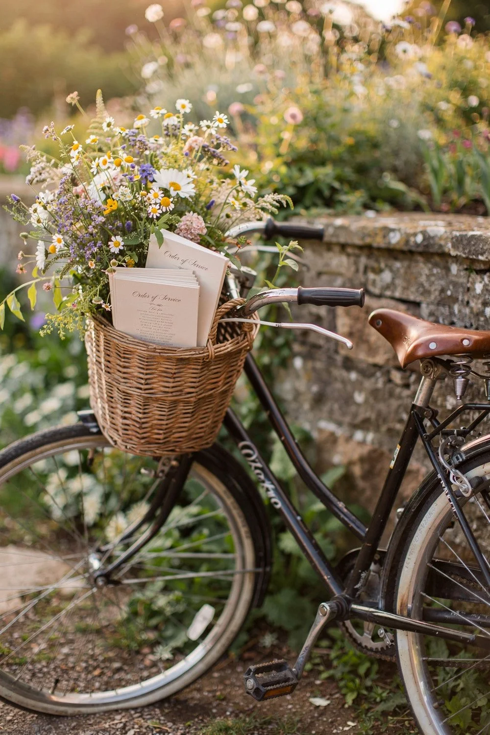 vintage bicycle with front basket filled with wildflowers and wedding programs