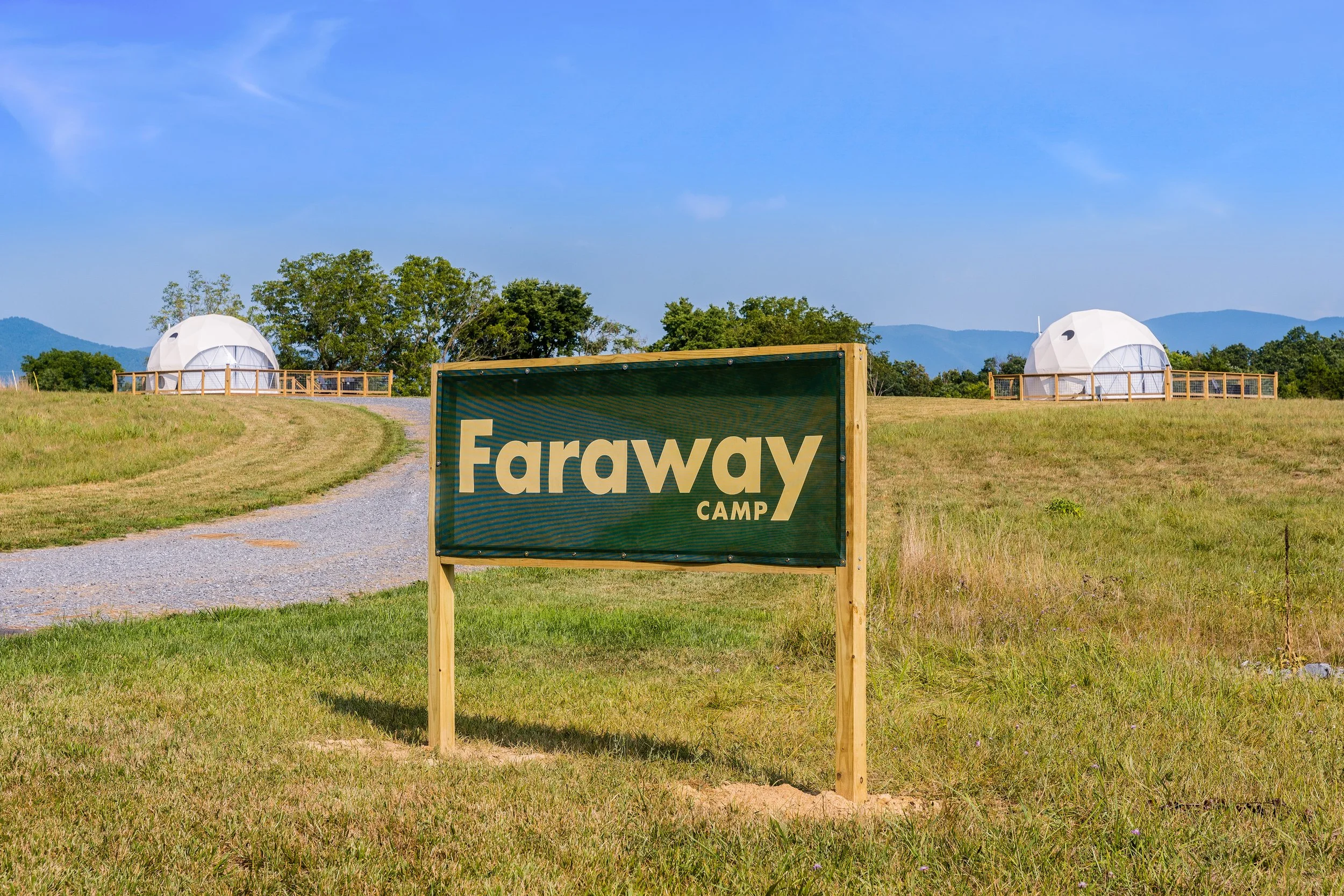 Sign for Faraway Camp in a grassy field with two white domed structures in the background under a blue sky.