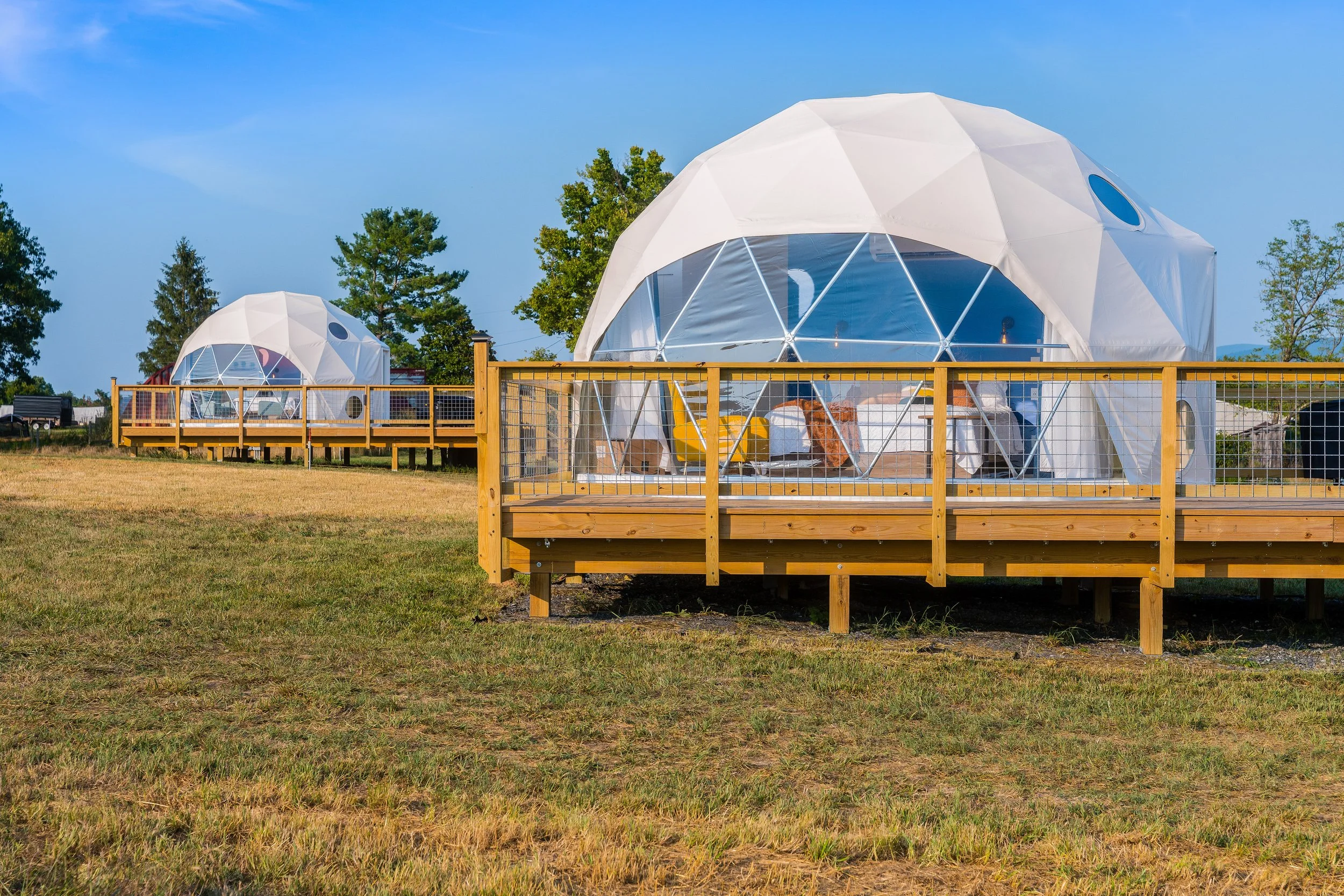 Geodesic dome tents on wooden decks in a grassy field, clear blue sky.