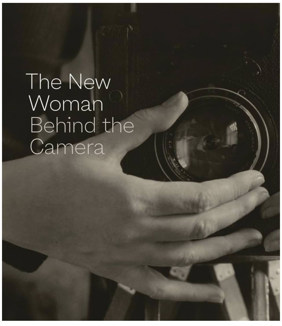 A person holding a camera with their fingers wrapped around the lens, reflected in the camera's glass.