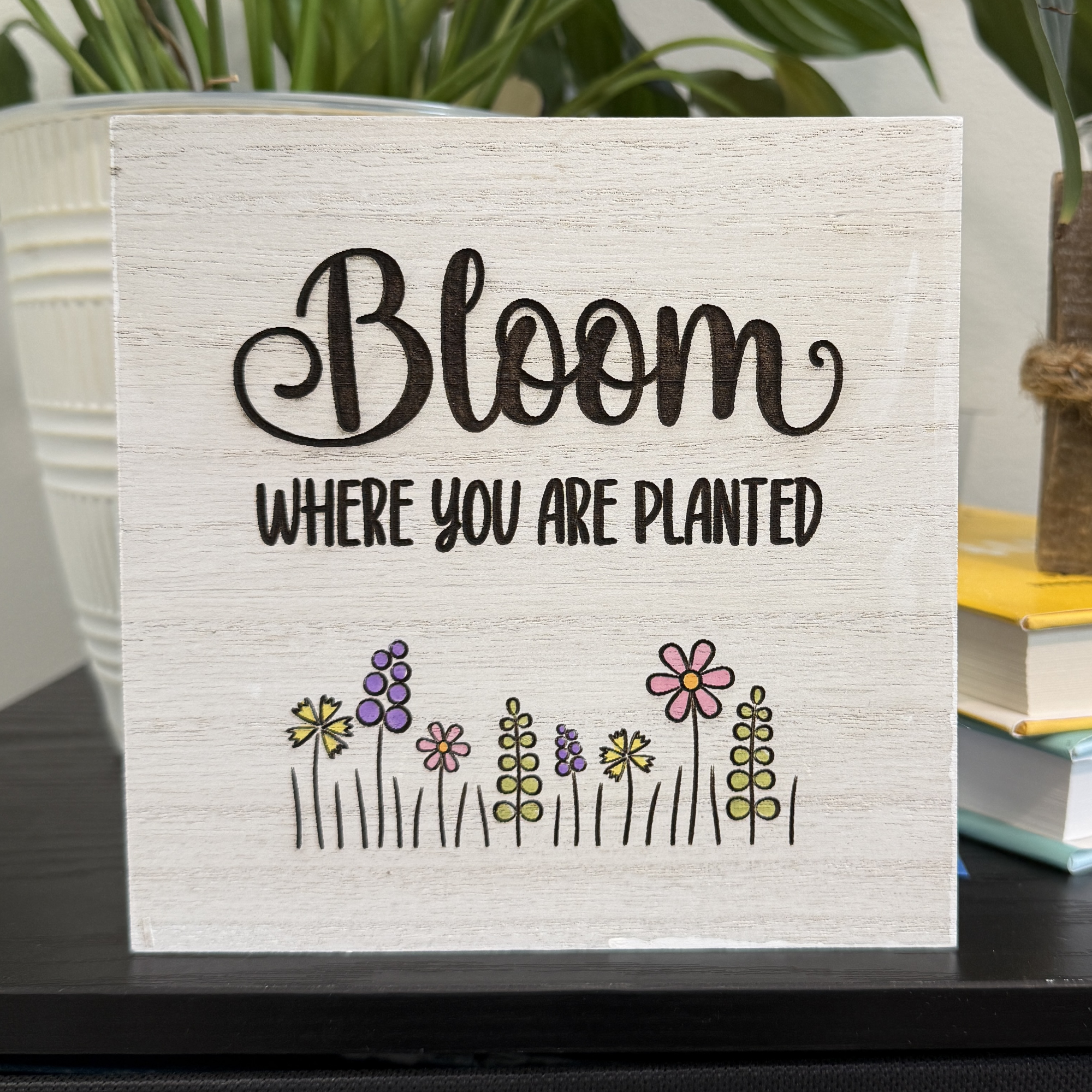 Bloom Where You Are Planted wood shelf sitter with hand-painted spring flowers displayed on a black shelf with white planter and greenery