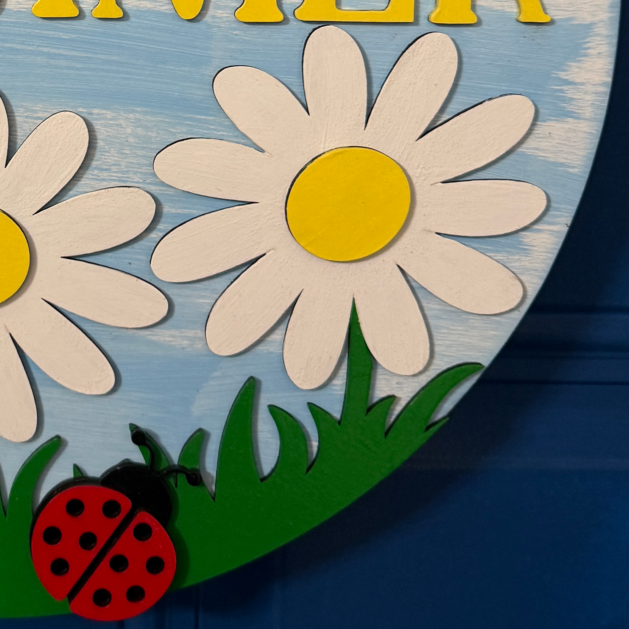 Bottom detail of summer door hanger with red ladybug accent resting in painted green grass