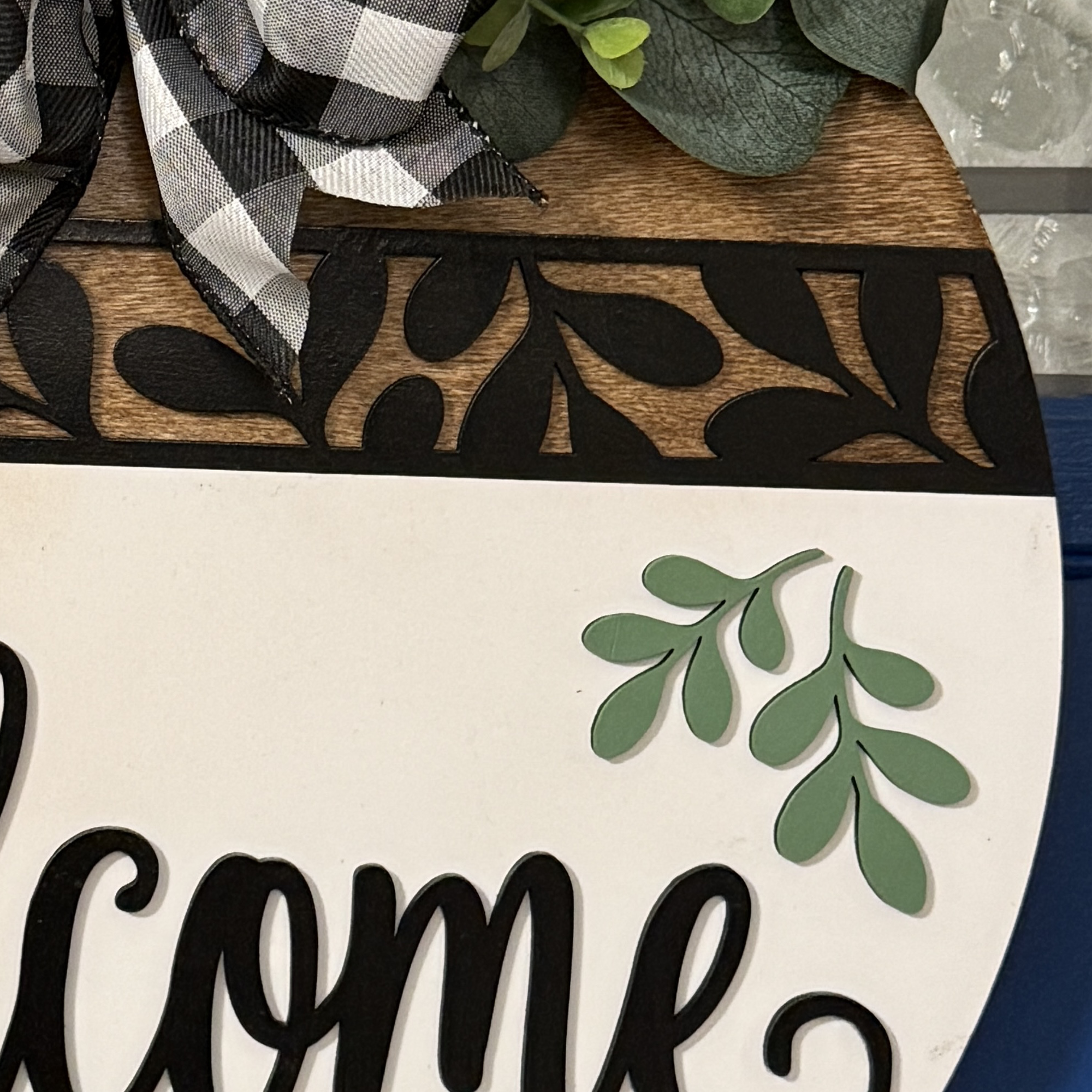Close-up of “Welcome” script lettering with black cutout leaf accents and faux greenery