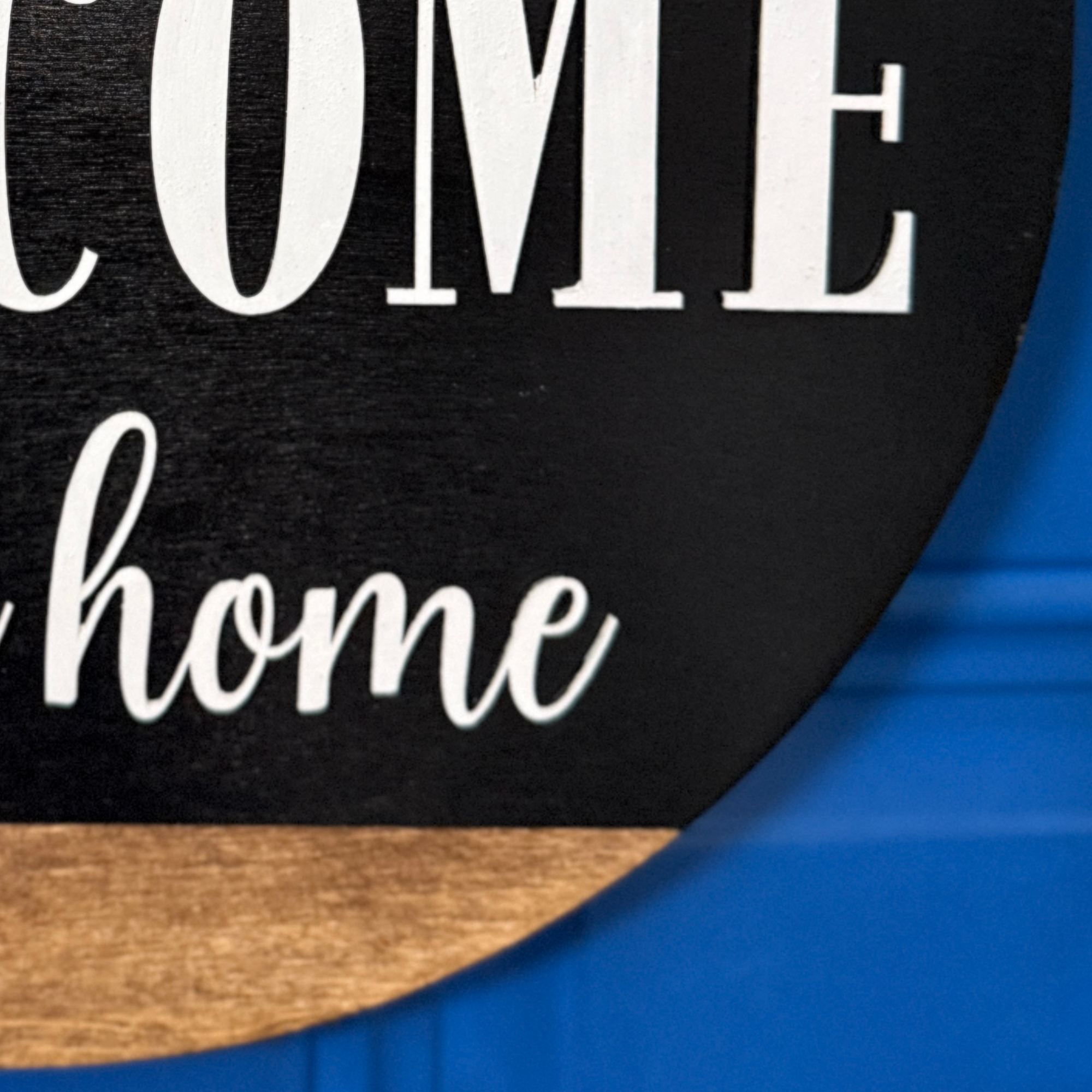 Close-up of white welcome to our home lettering on black painted wood door hanger with natural wood accent