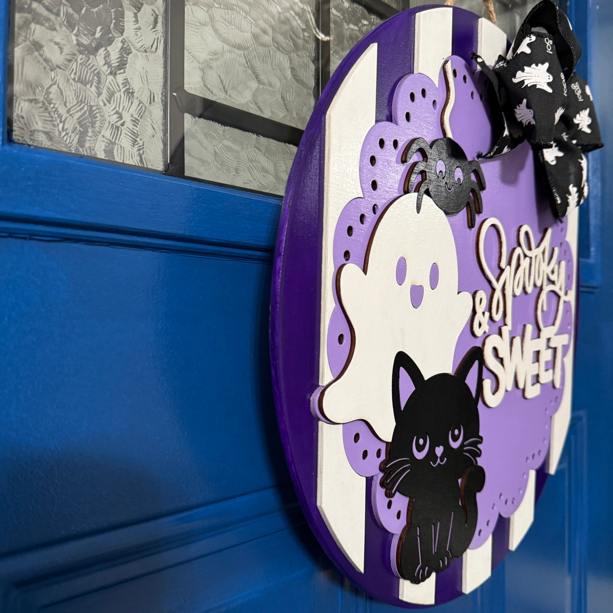 Side angle of purple Spooky and Sweet Halloween door hanger showing dimensional layered wood ghosts, black cat, and bow