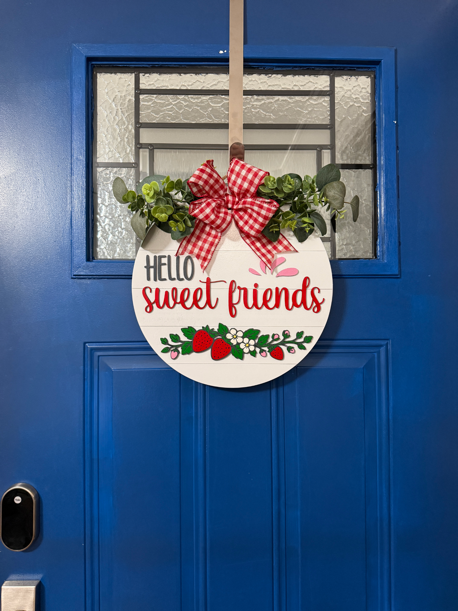 Full view of Hello Sweet Friends strawberry door hanger displayed on bright blue front door with red gingham bow