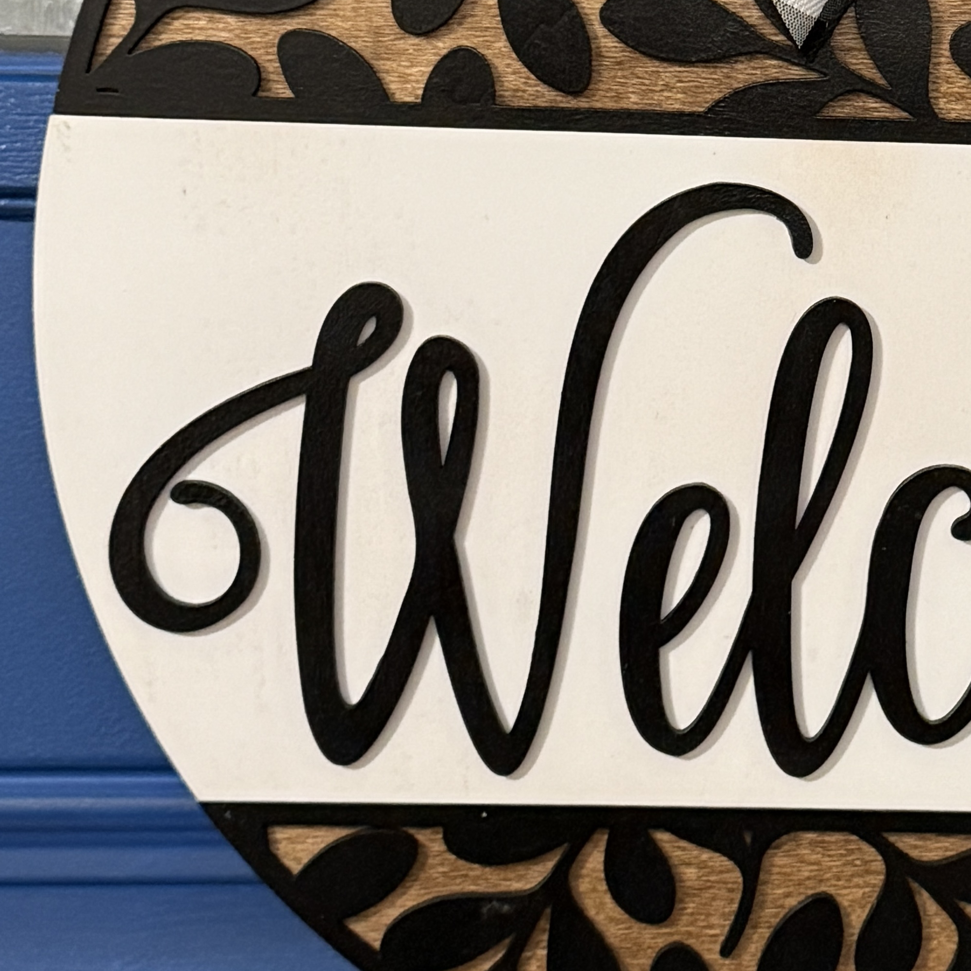 Close-up of “Welcome” script lettering with black cutout leaf accents and faux greenery