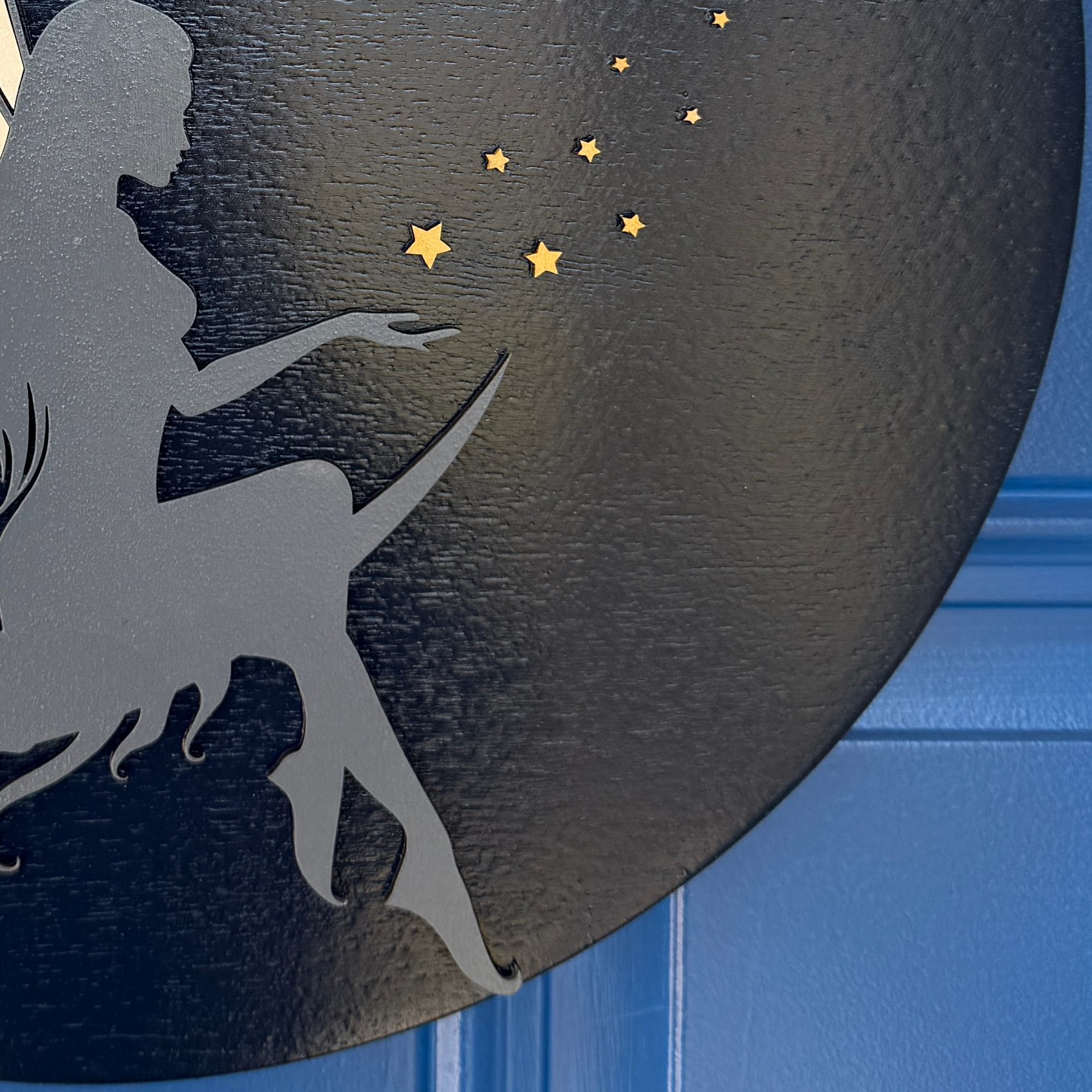 Close-up of fairy silhouette with star accents on black round wood door hanger