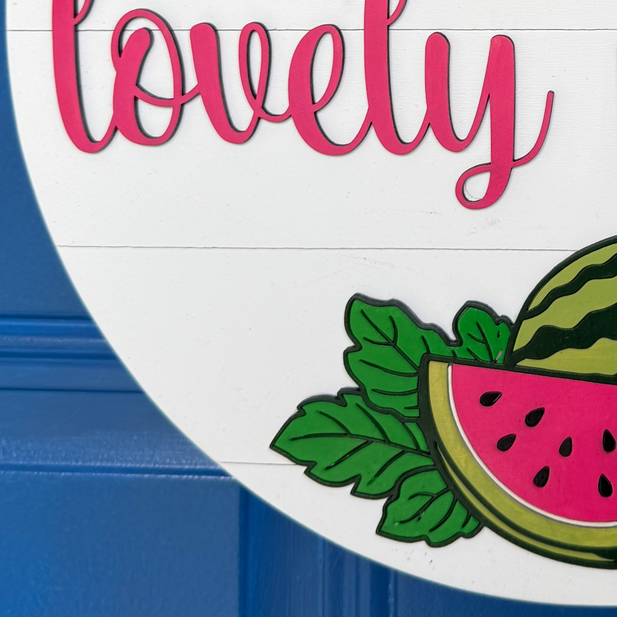 Close-up of layered wood watermelon slice and greenery on a handmade Hello Lovely People door hanger.