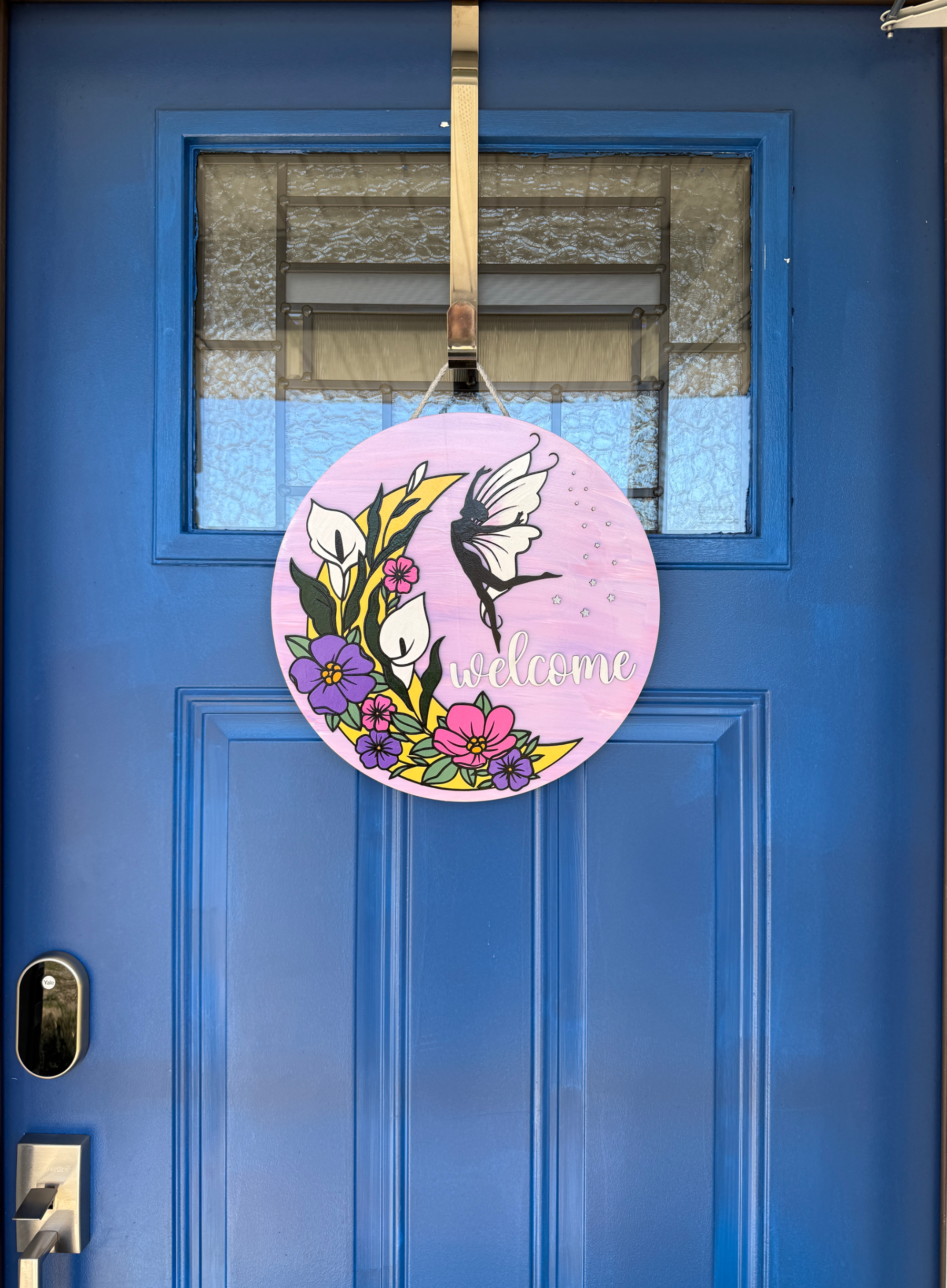 Wide shot of 14 inch round pink fairy welcome wood door hanger displayed on blue front door