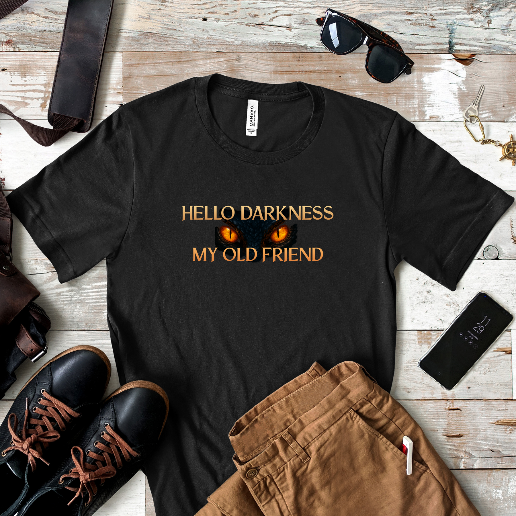 Flat lay of black “Hello Darkness My Old Friend” shirt styled with boots, pants, sunglasses, and accessories.