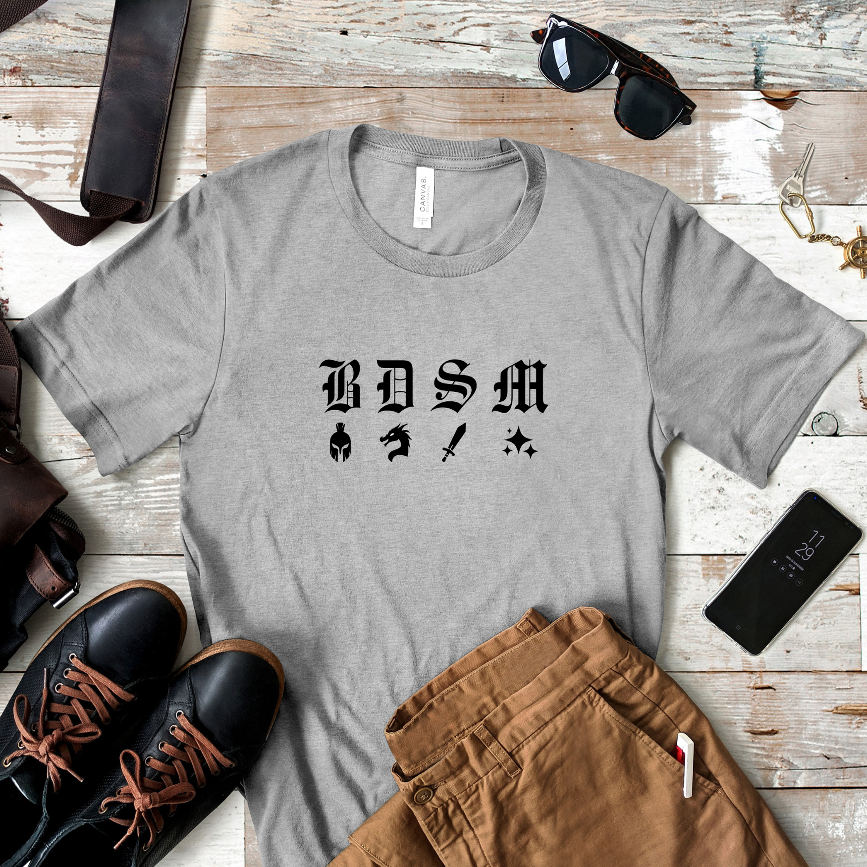 Heather gray t-shirt with black fantasy BDSM lettering and icons shown in rustic flatlay