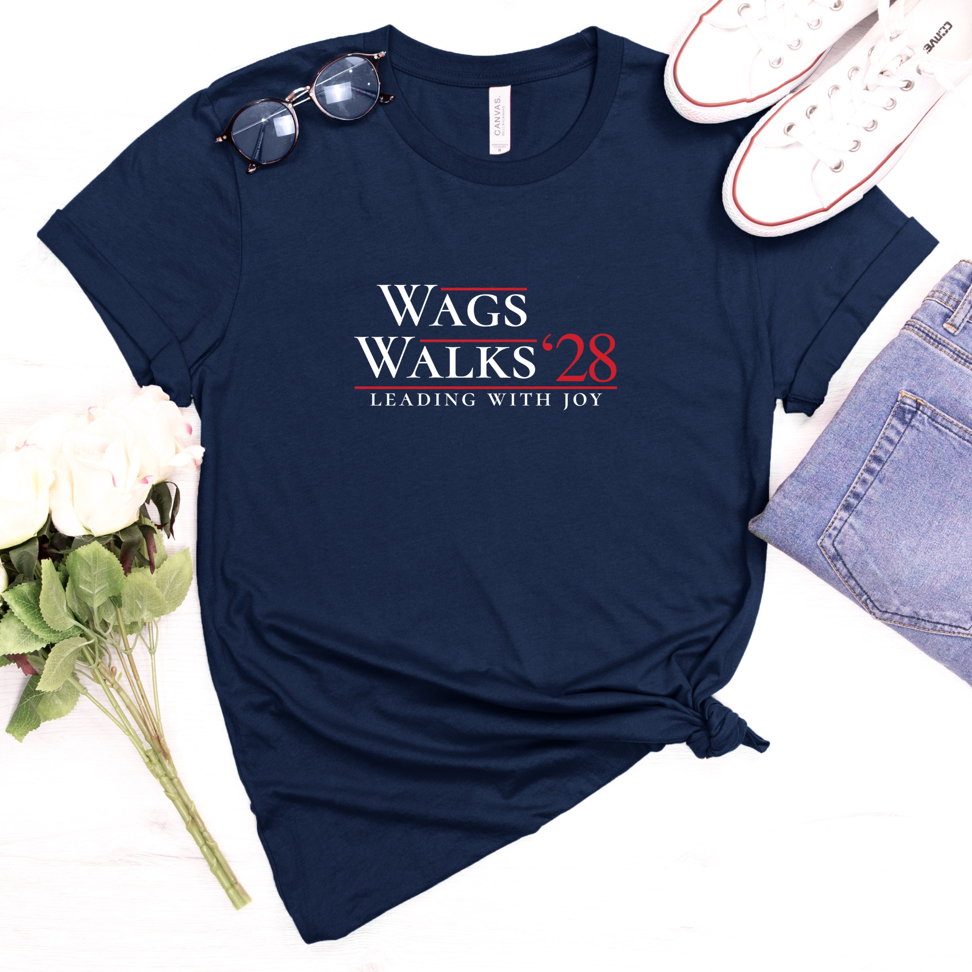 Navy Wags Walks ’28 parody campaign shirt displayed with jeans, flowers, and casual accessories.