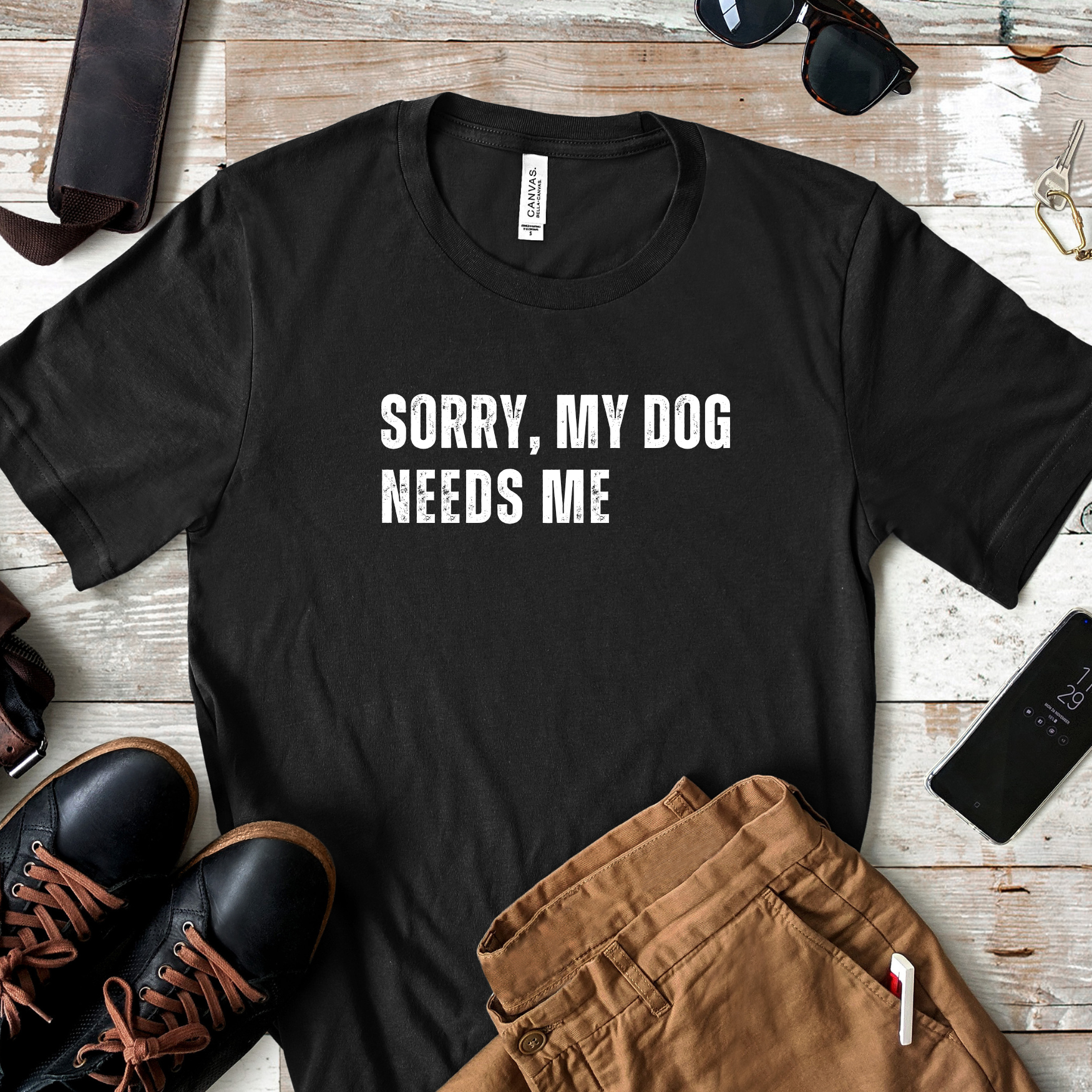 Flat lay of black dog lover t-shirt with “Sorry, My Dog Needs Me” text styled with shoes and accessories