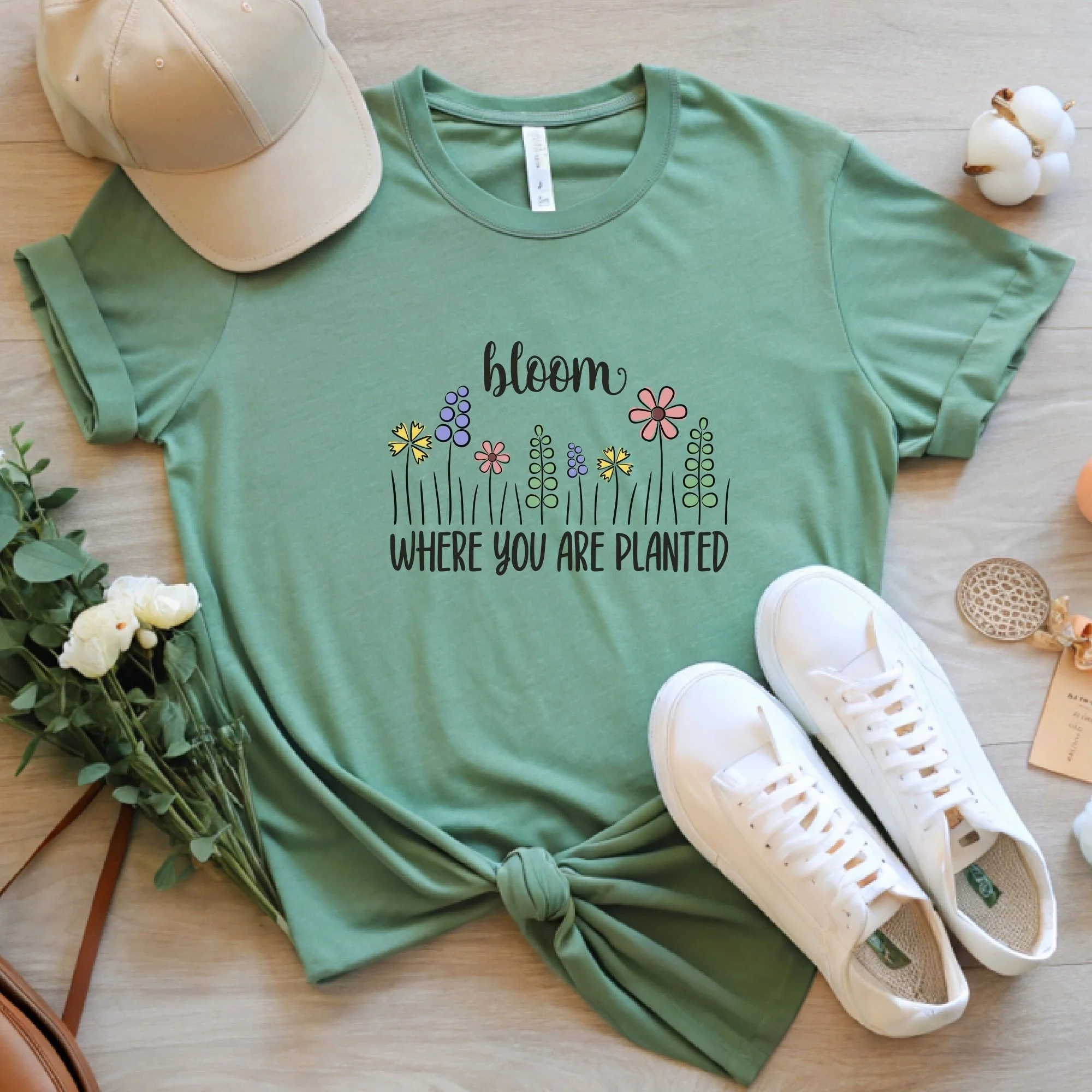 Daytime styled view of Bloom Where You Are Planted graphic shirt on sage green tee with jeans, sneakers, and spring accessories