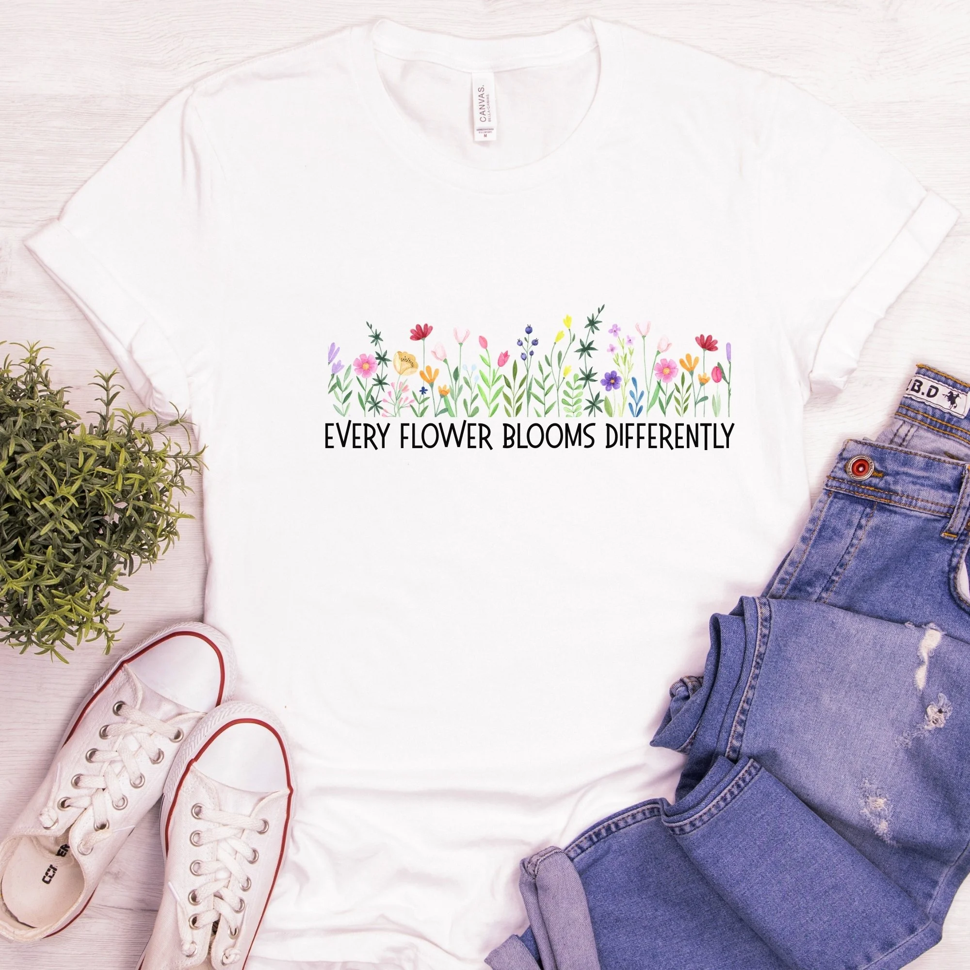 Daytime styled view of Every Flower Blooms Differently graphic shirt on white tee with jeans, sneakers, and spring accessories
