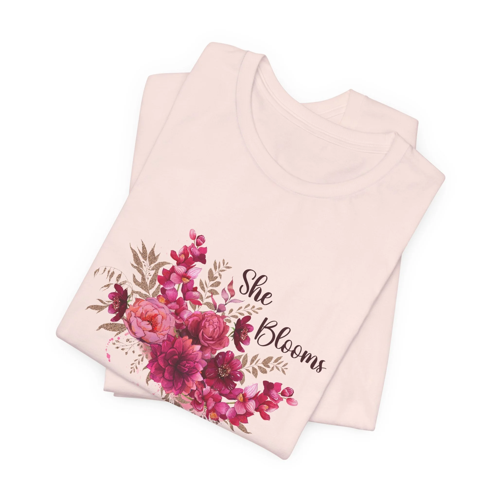 Folded soft pink t-shirt featuring She Blooms graphic