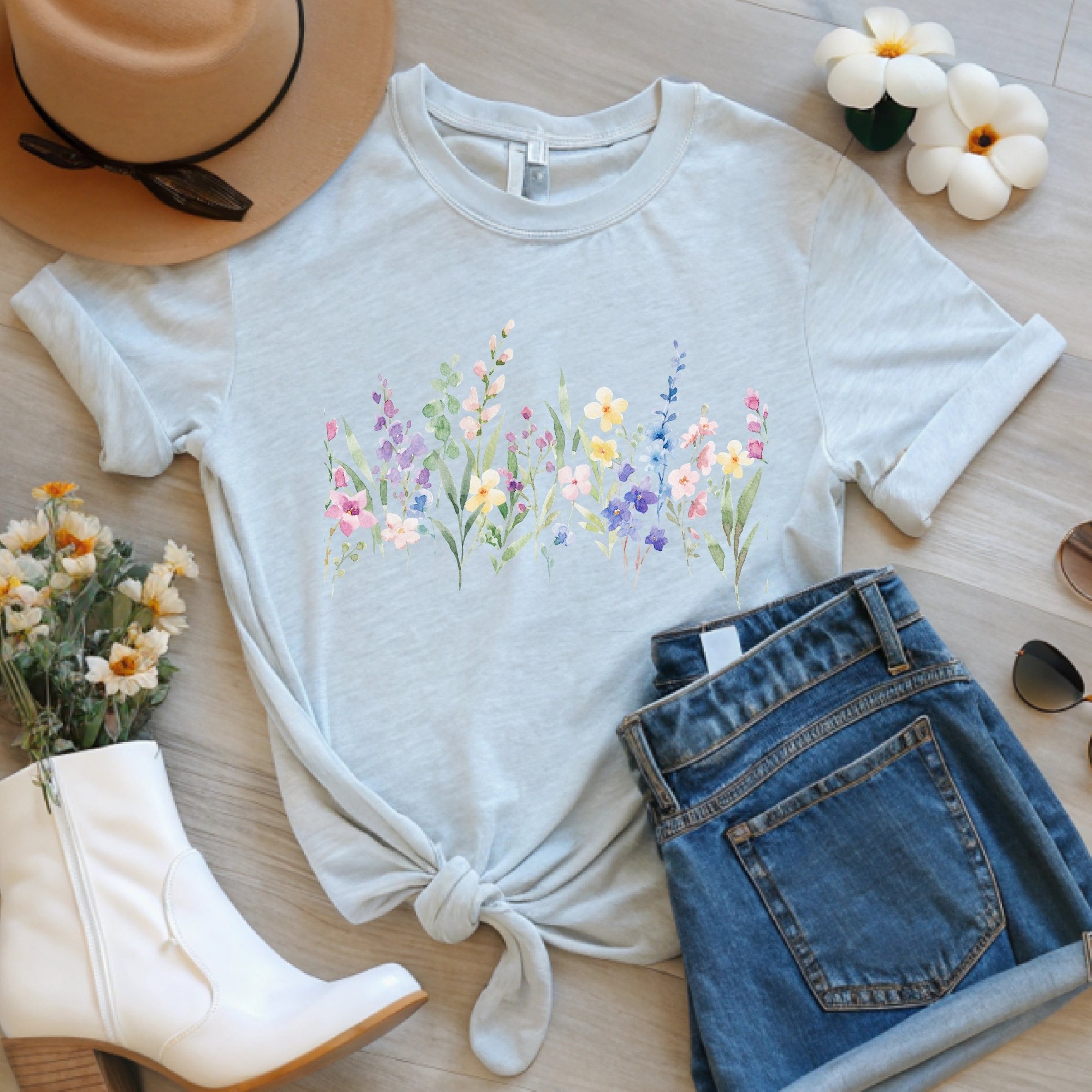 Daytime styled view of pastel watercolor wildflower border shirt on an Ash colored tee with jeans, hat, and spring accessories