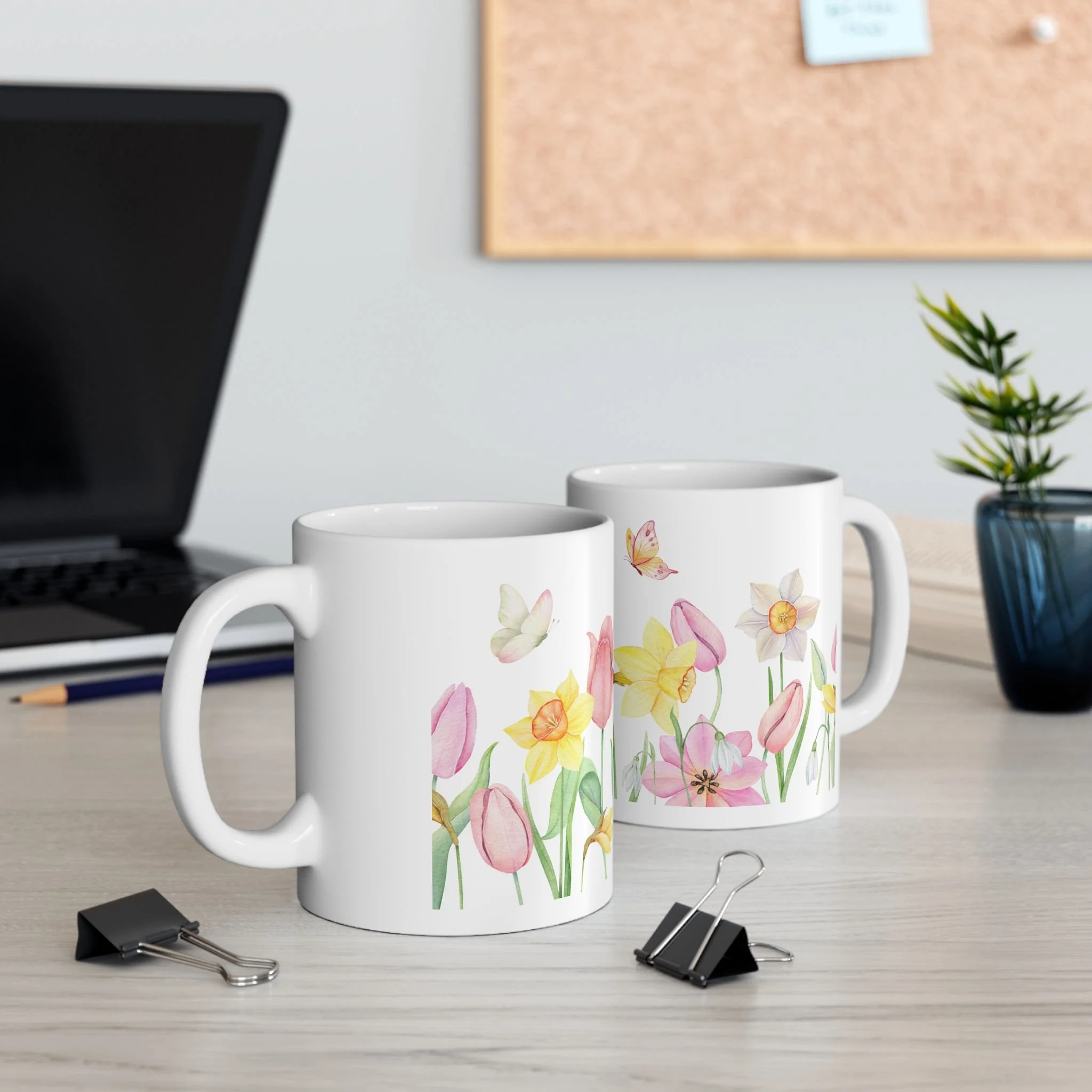 Styled desk scene with two spring floral mugs featuring tulips, daffodils, and butterfly accents
