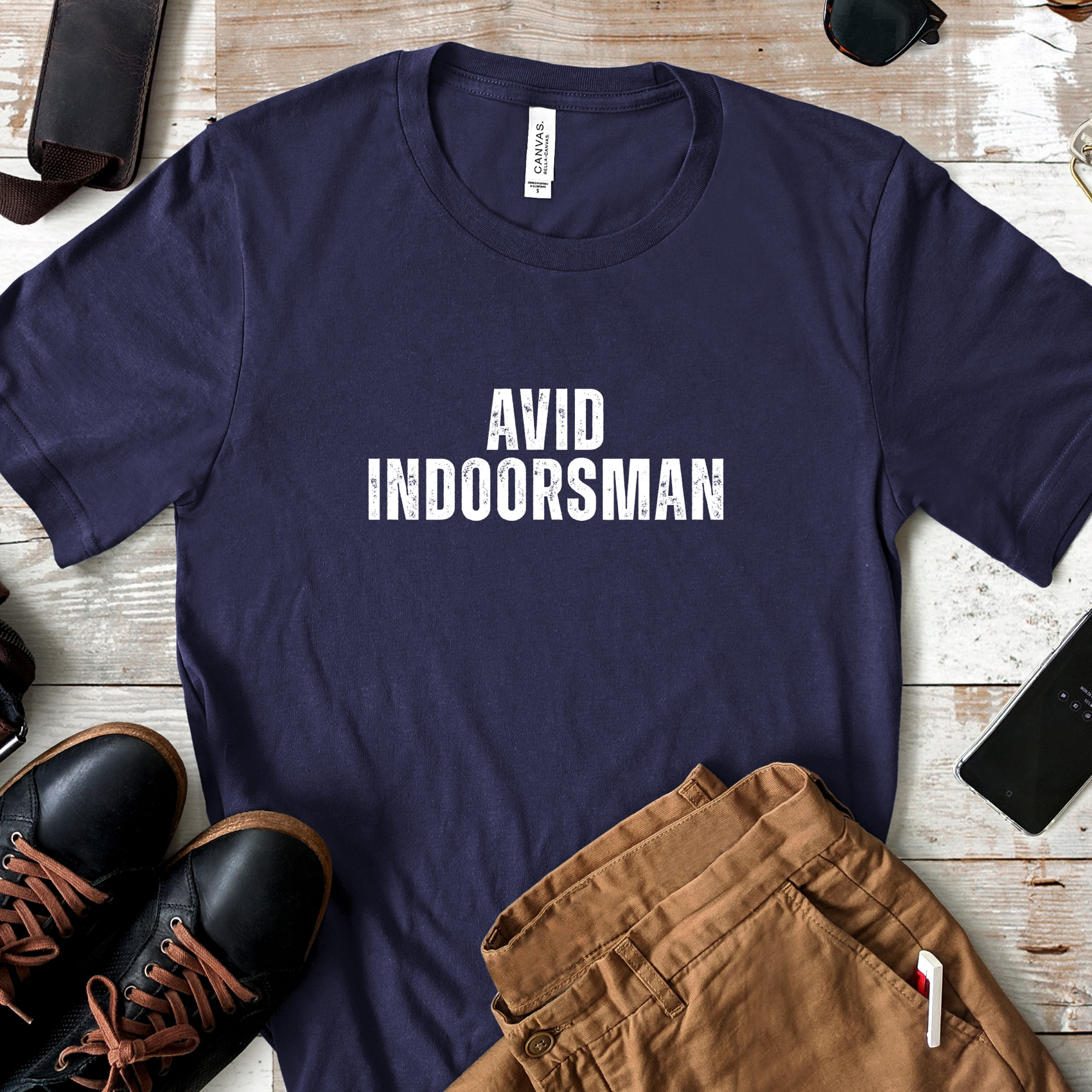 Avid Indoorsman graphic t-shirt in navy laid flat with casual outfit including brown pants and black shoes on rustic wood background