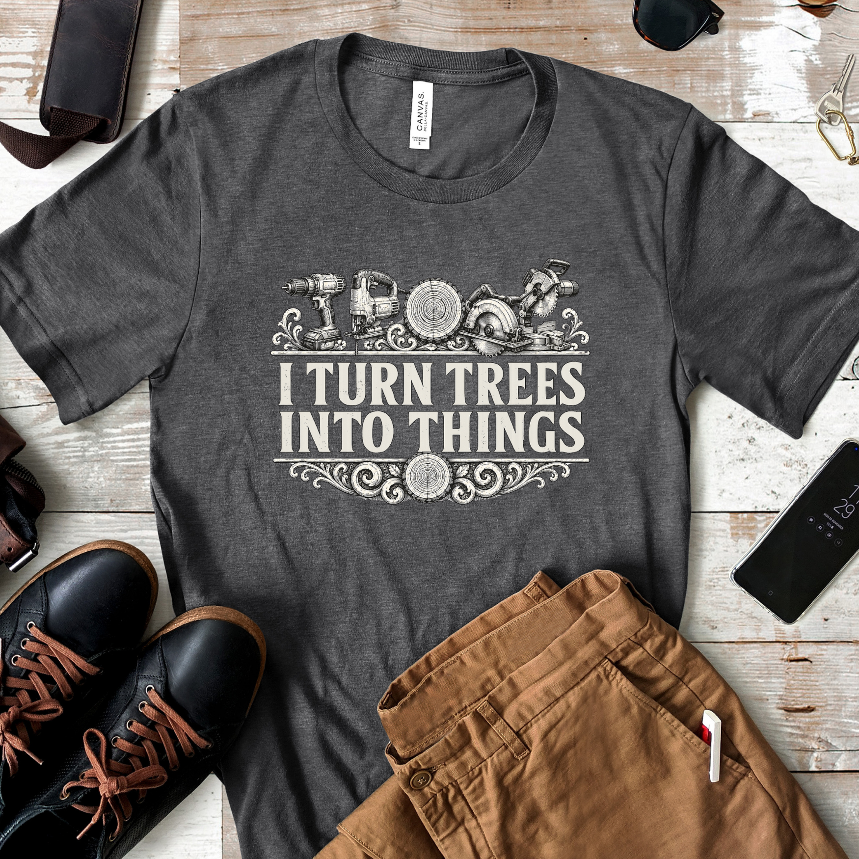 Gray "I Turn Trees Into Things" woodworking t-shirt flat lay with work boots and carpenter pants