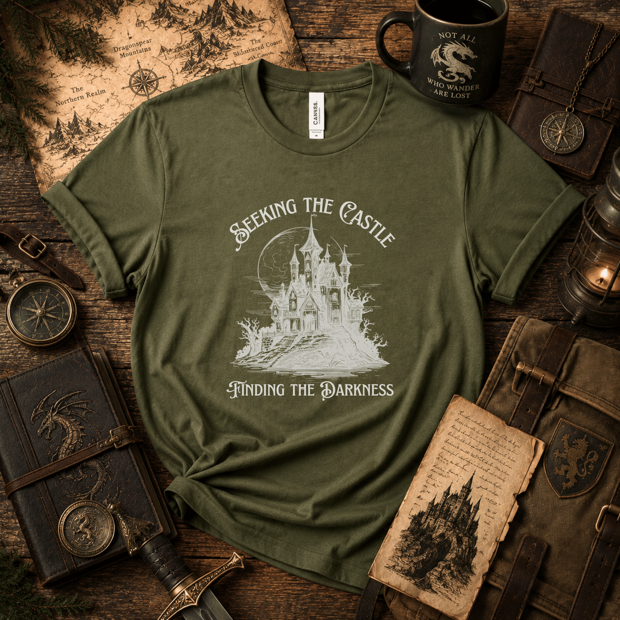 Lifestyle mockup of an Olive Bella+Canvas fantasy castle t-shirt styled with antique maps, books, lanterns, a mug, and other adventure-inspired props.