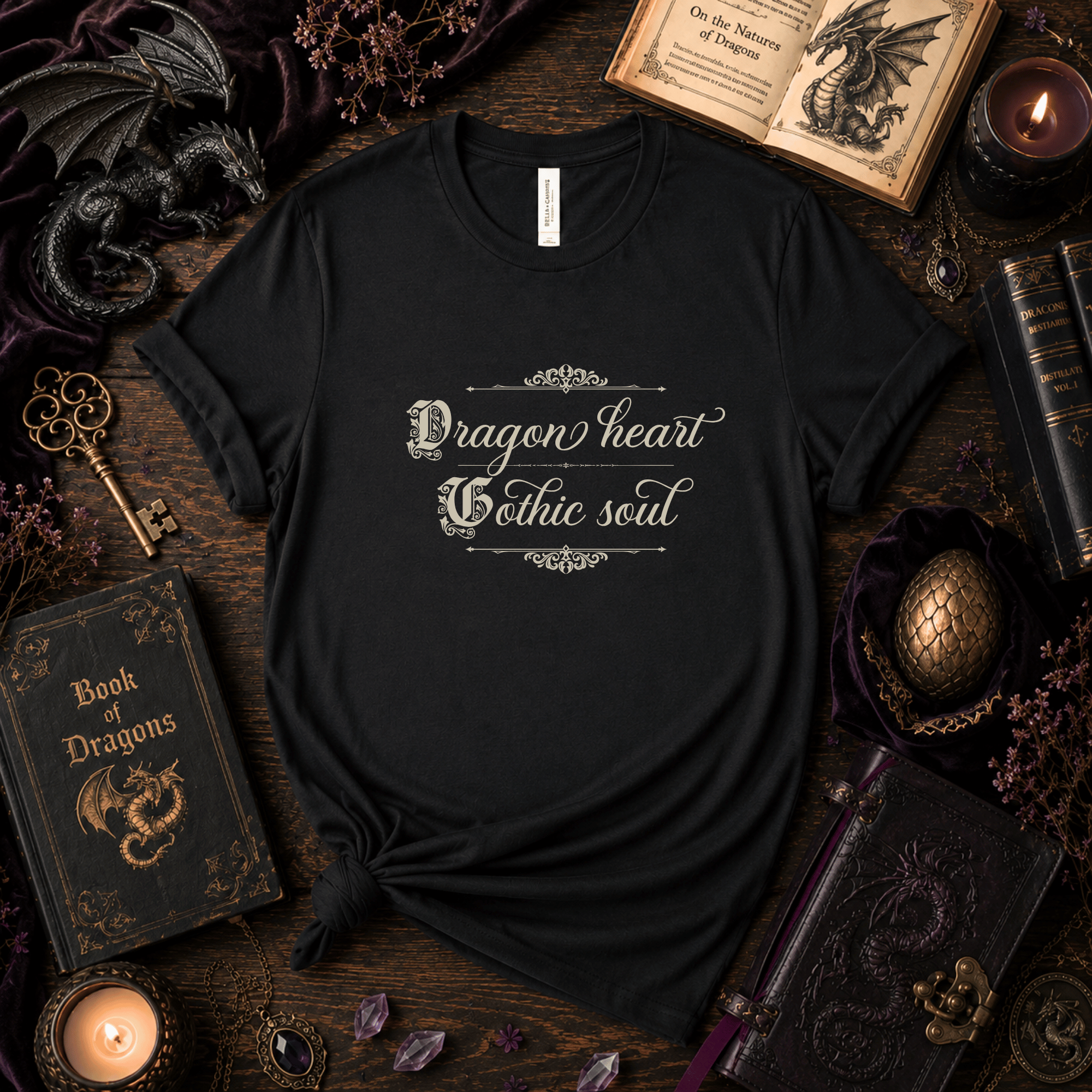Lifestyle mockup of a Black Bella+Canvas "Dragon Heart, Gothic Soul" fantasy t-shirt styled with antique books, candles, dragon-themed décor, and dark academia accessories.