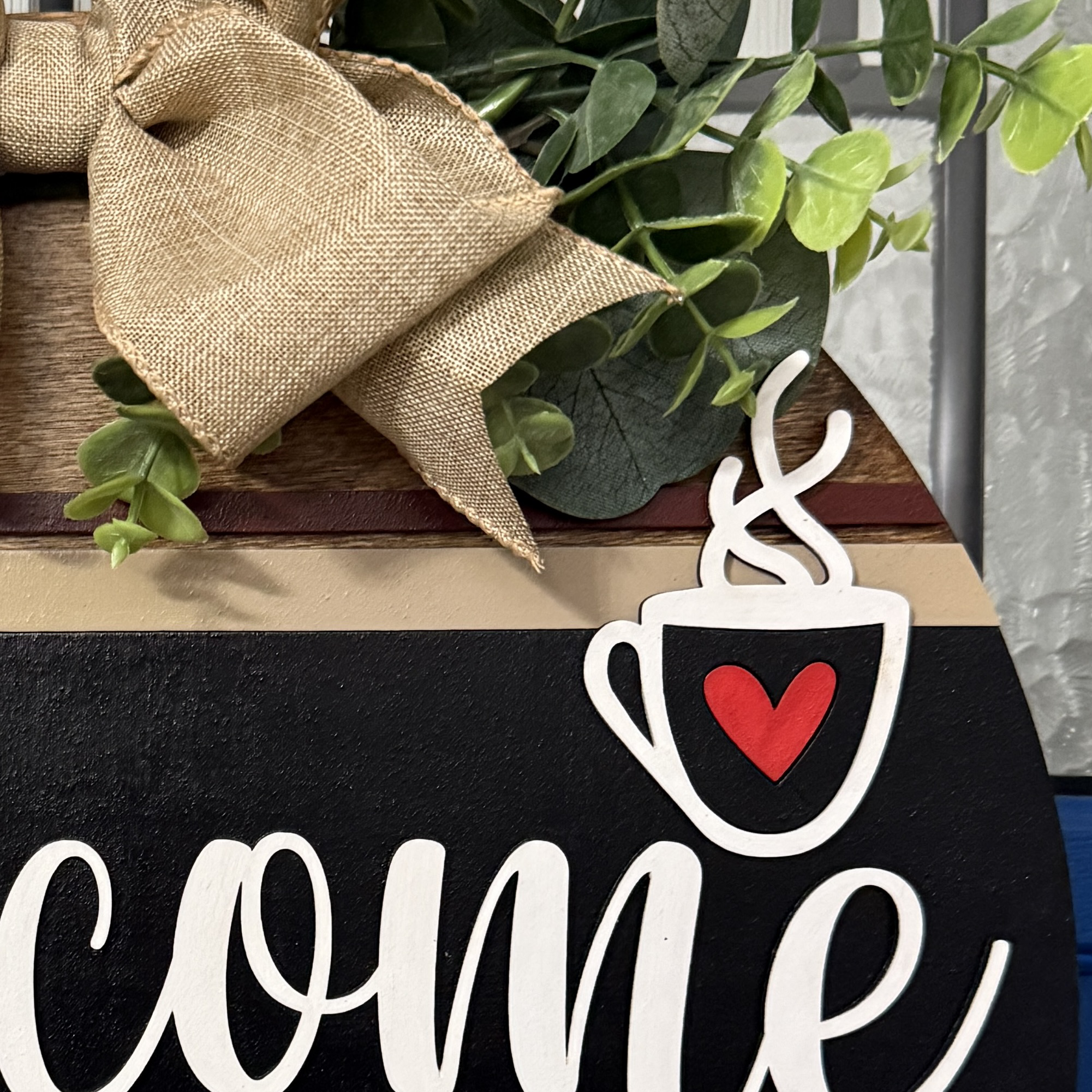 Detailed view of faux linen bow and greenery accent at top of door hanger